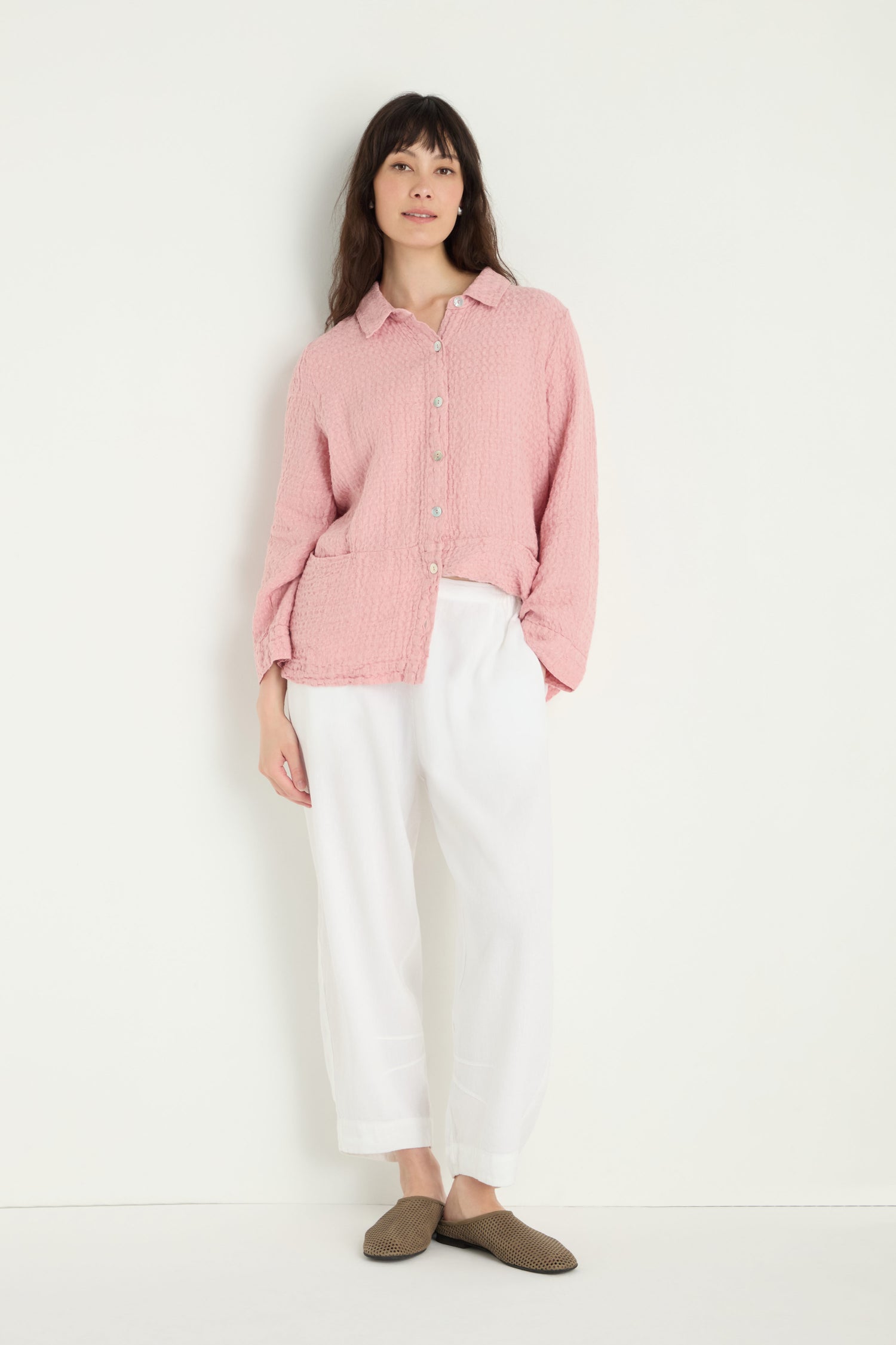 A person stands against a plain white background wearing a pink button-up shirt, Twisted Linen Crop Bubble Trouser, and brown slippers.