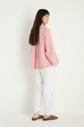 A woman stands sideways against a plain white background, wearing a textured pink sweater, Twisted Linen Crop Bubble Trousers for a breathable feel, and brown slip-on shoes.