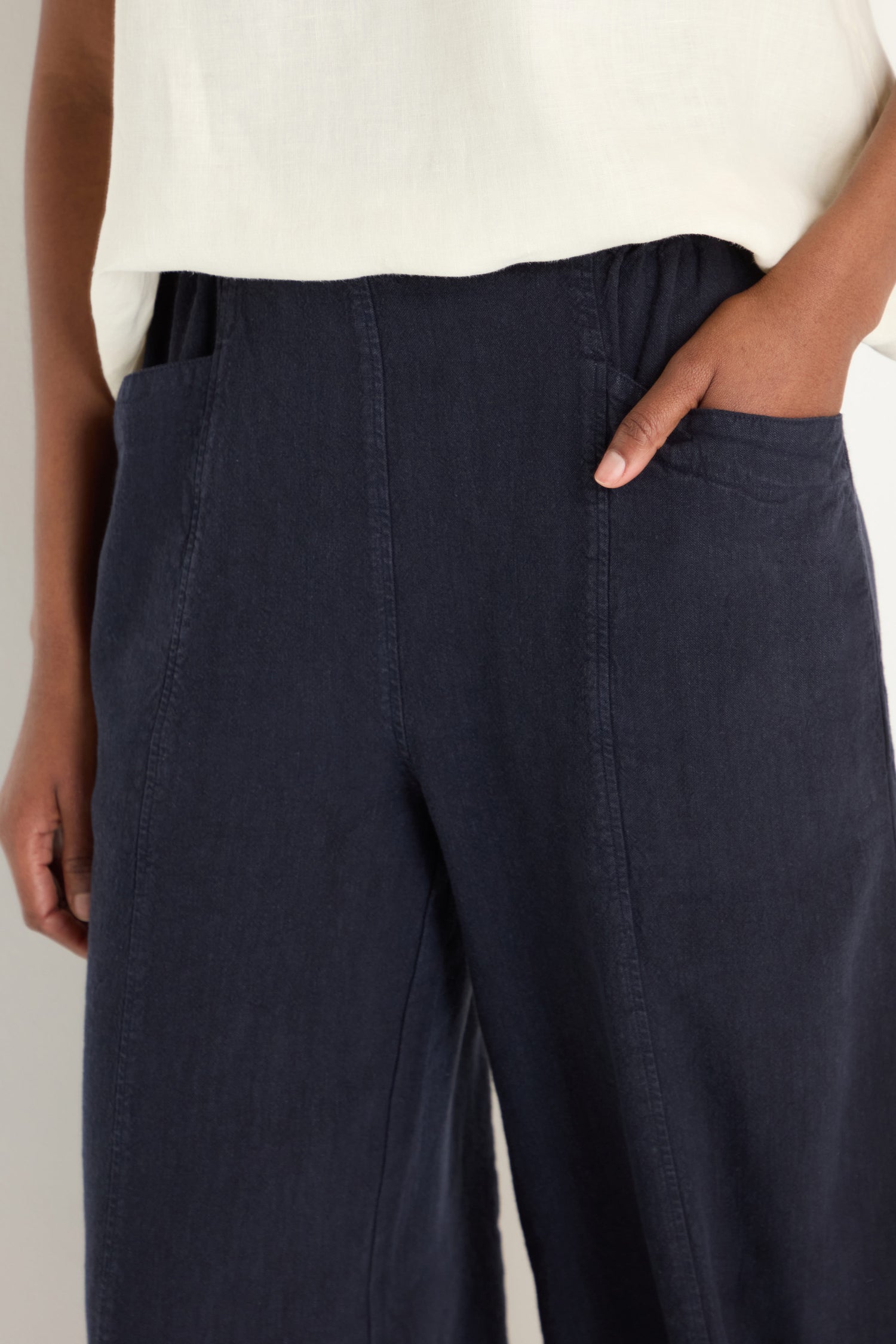 A person wearing Twisted Linen Bubble Trousers in dark blue, crafted from breathable linen, paired with a white top stands with one hand in their pocket.