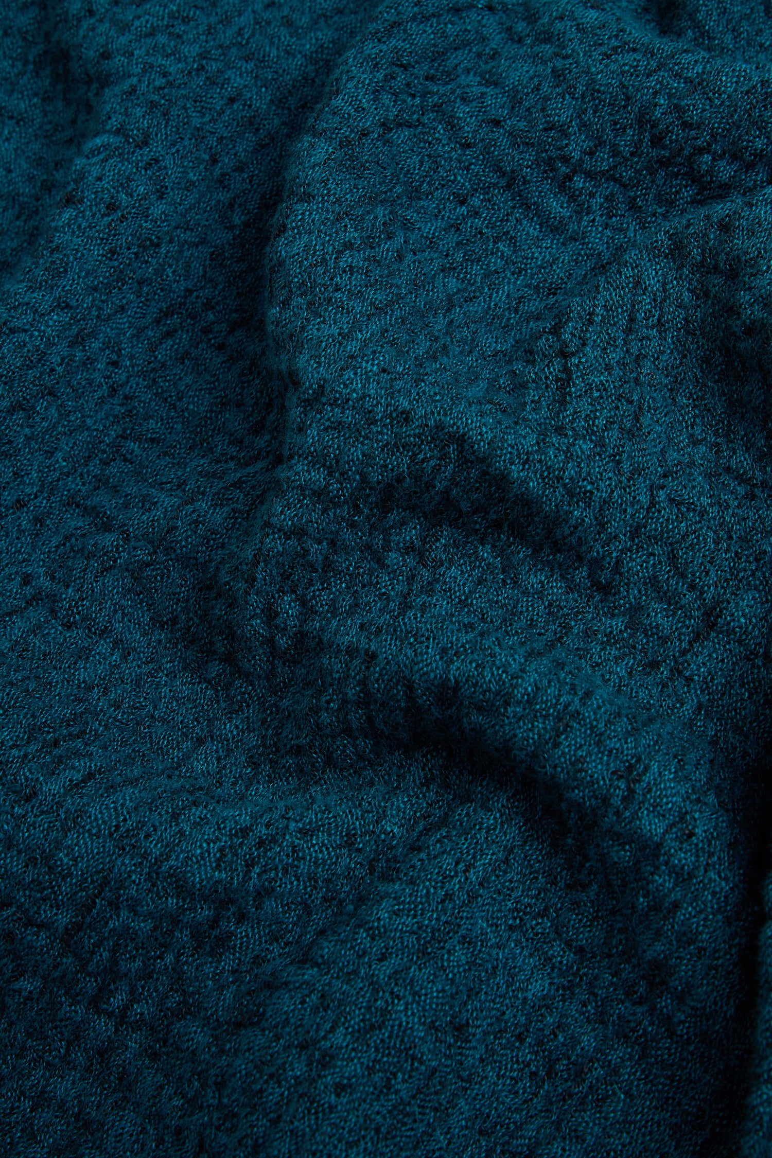 Close-up view of textured, dark teal fabric with visible folds and raised patterns, as featured in the Crinkle Linen Blend Bubble Trousers.
