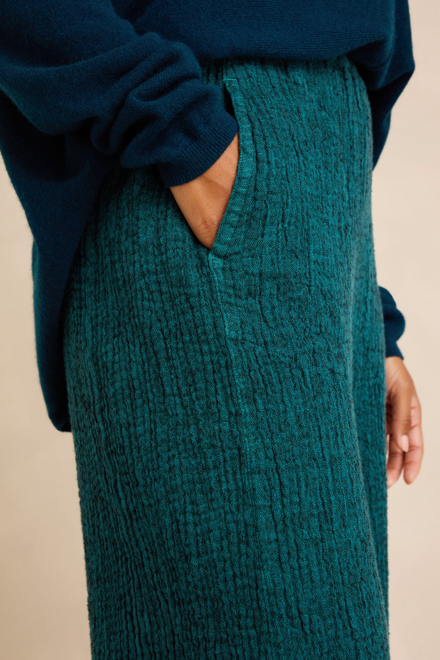 A person wearing Crinkle Linen Blend Bubble Trousers in dark teal with a hand in the pocket, paired with a navy blue sweater.