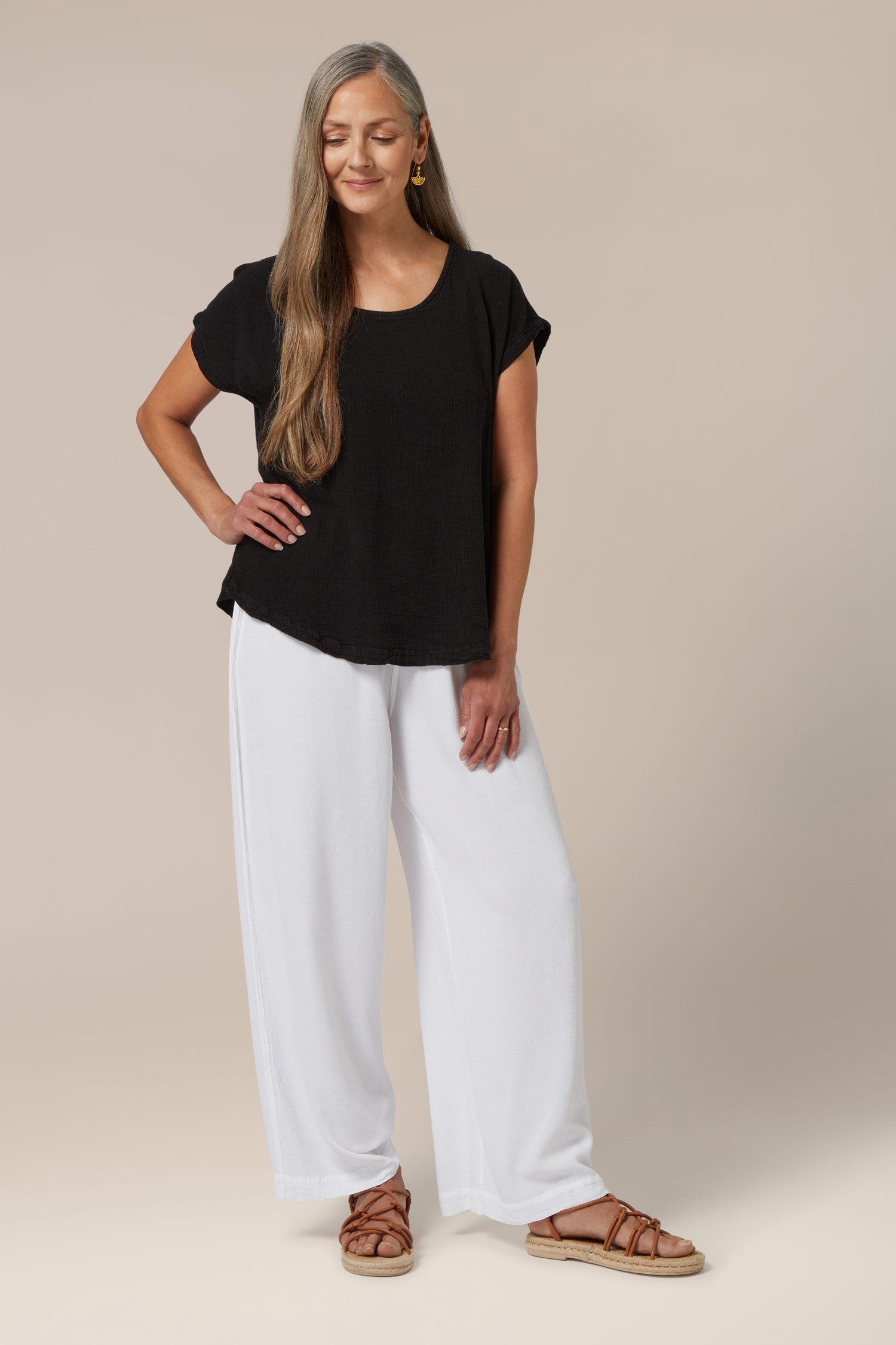 Sentence with the product name substituted: Woman wearing a warm weather look with a black Paula Crinkle Linen Top, white trousers, and brown sandals.