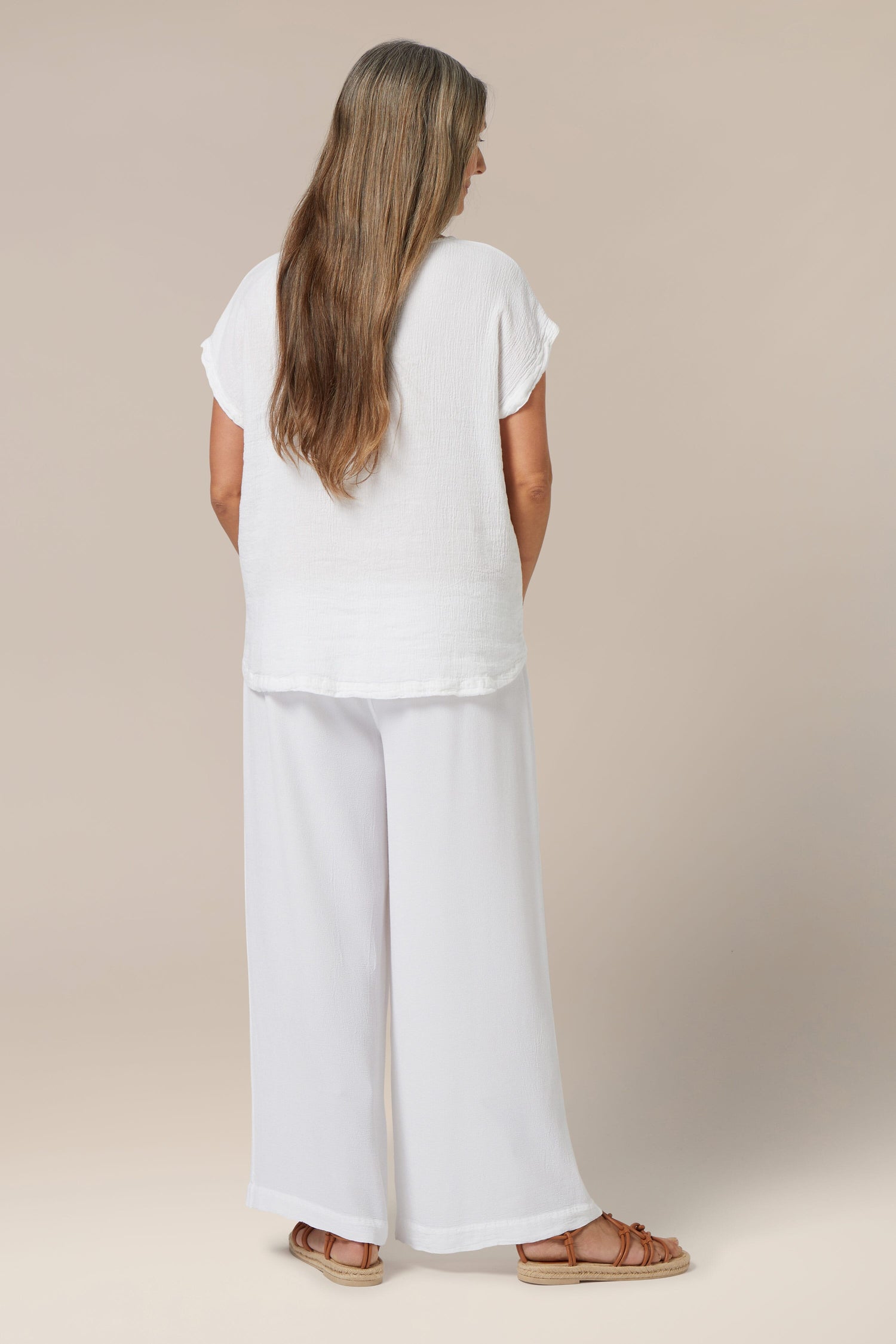 Woman standing facing away from the camera, wearing a Grace Crinkle Linen Top and wide-leg pants, with long hair down her back.