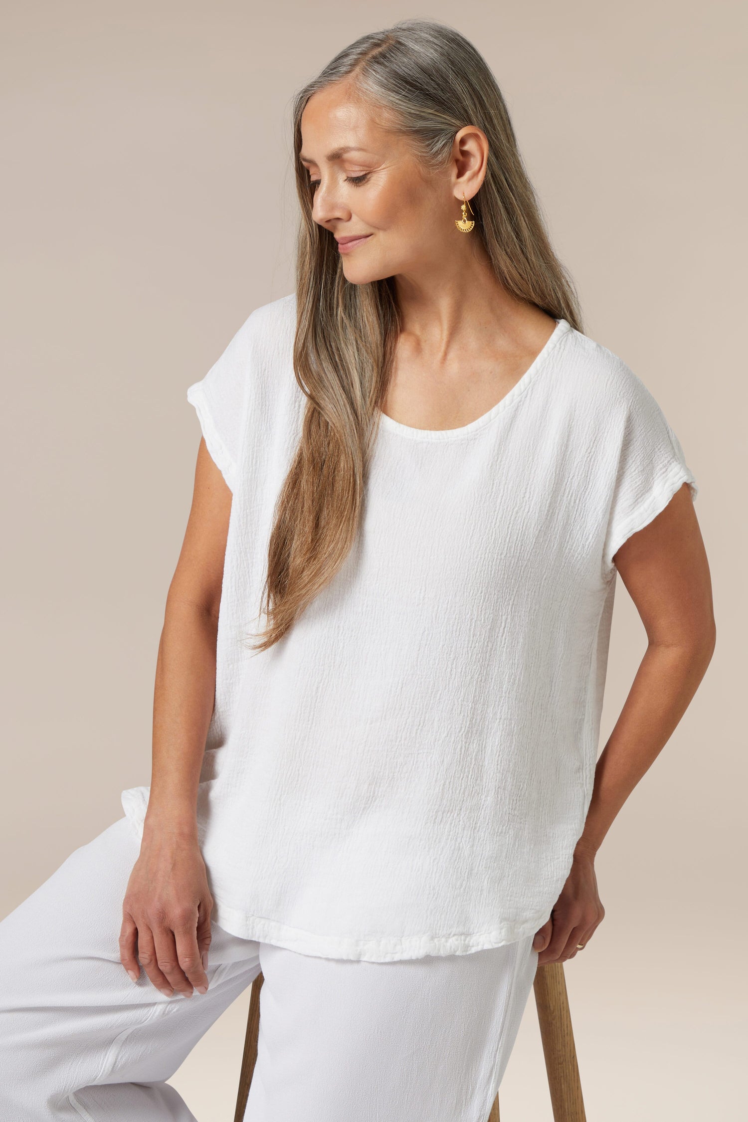 Woman in white <Product Name> sitting and looking to the side.