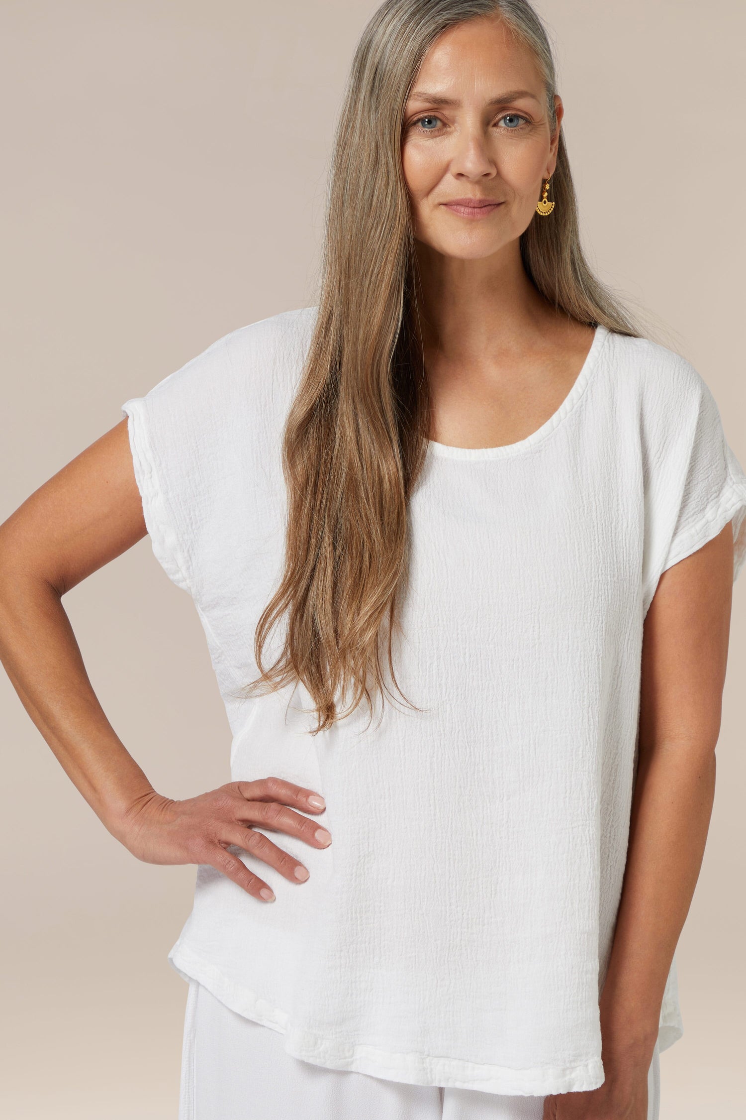 A woman with long grey hair wearing a Aegean Crinkle Linen Top and a single earring, posing with her hand on her hip.