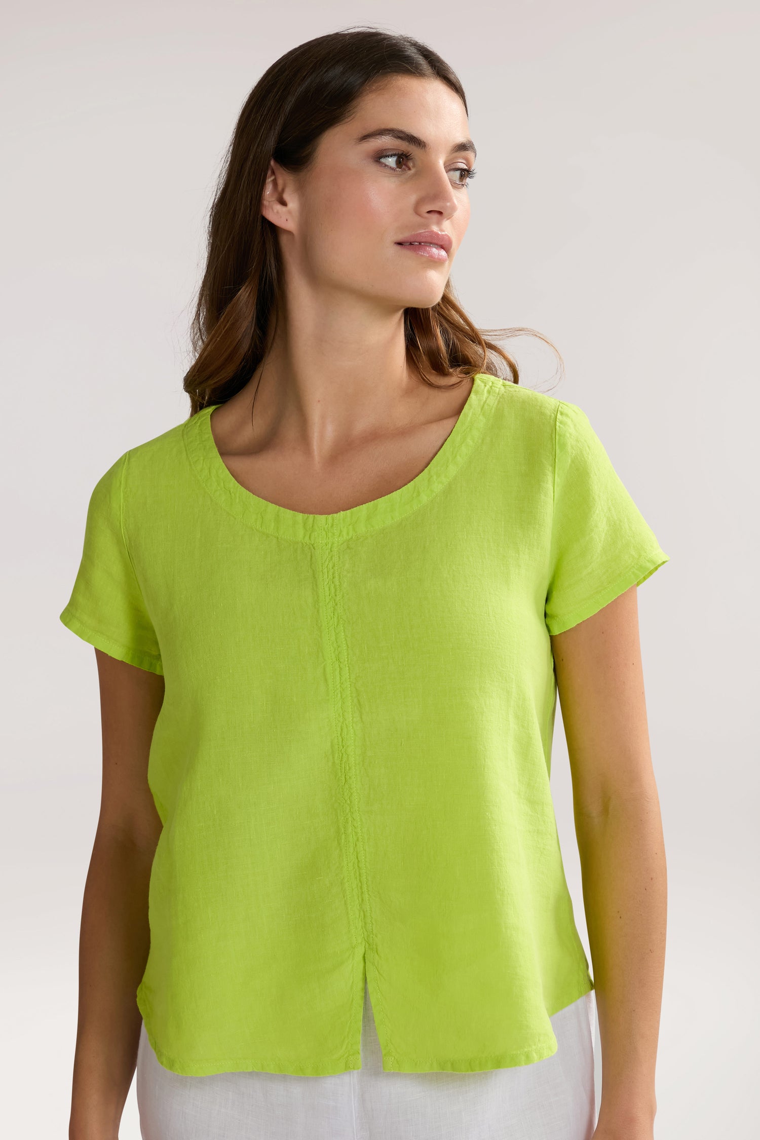 Woman wearing a Slit Hem Linen Top in bright green and white pants, looking off to the side against a plain background.