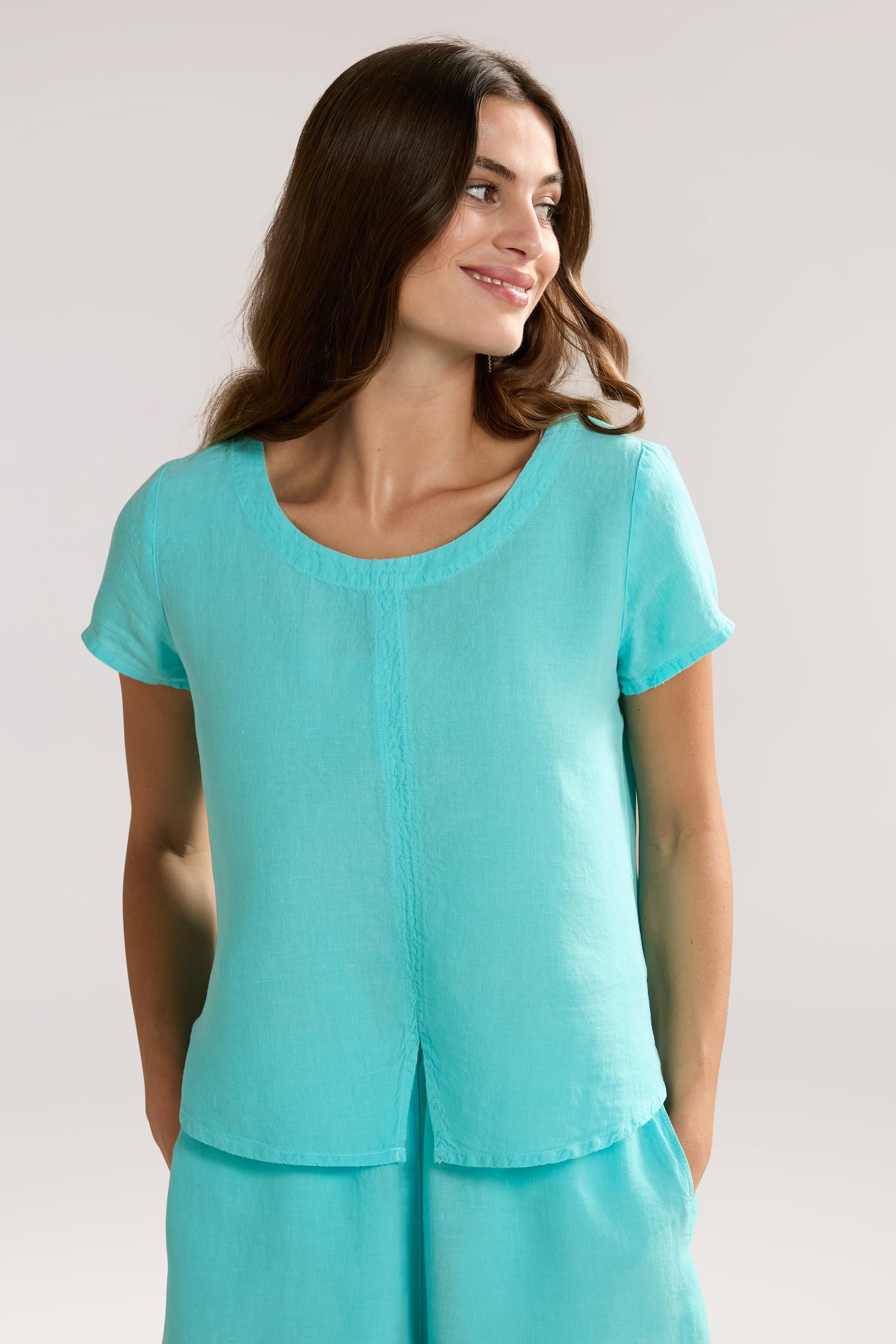 Person wearing a Slit Hem Linen Top with a round neckline, looking to the side with a neutral expression. Background is light and plain.