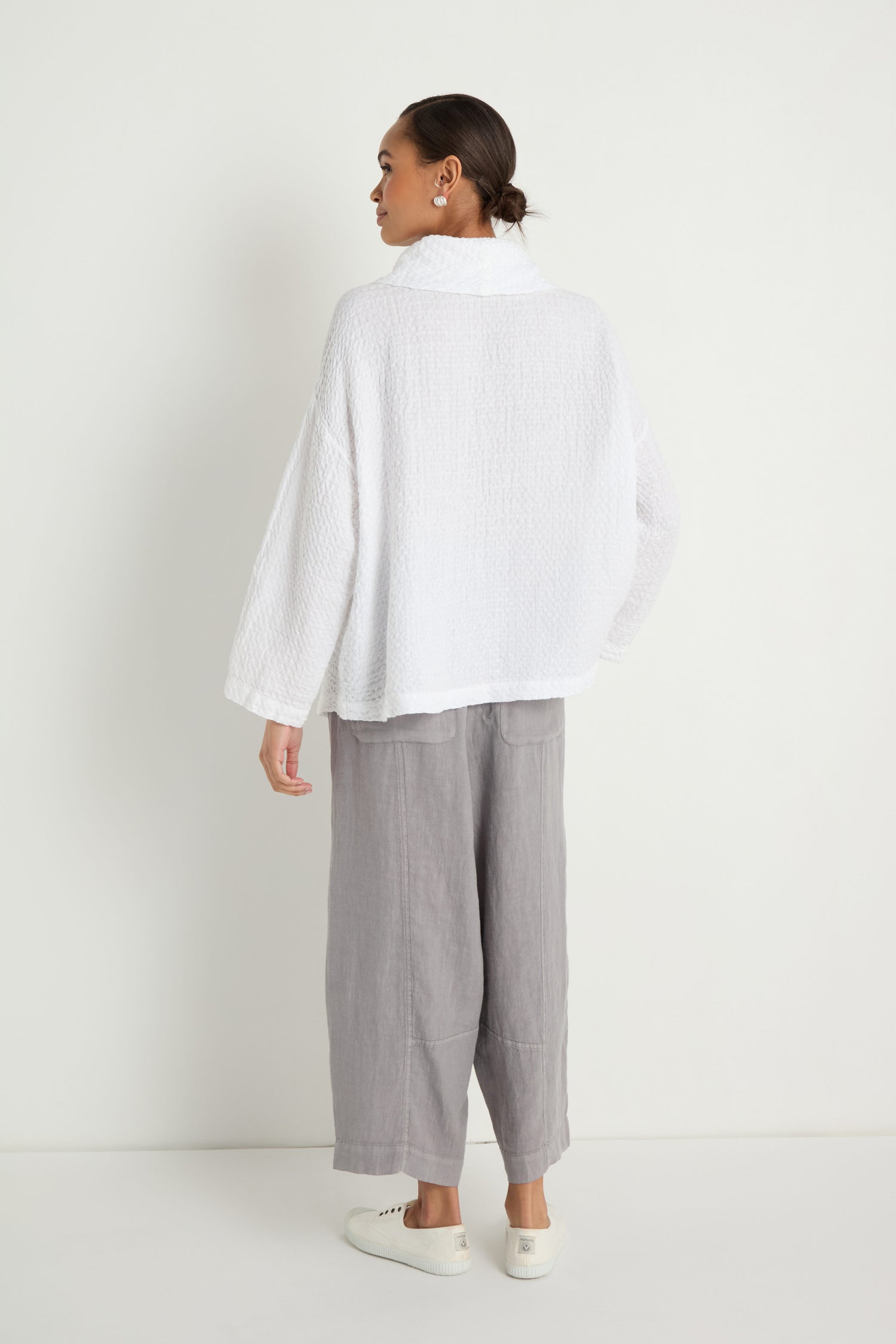 A woman, facing away, wears the Waffle Linen Boxy Cowl Neck Top with a relaxed fit, paired with light gray wide-leg pants and white sneakers against a plain white background.