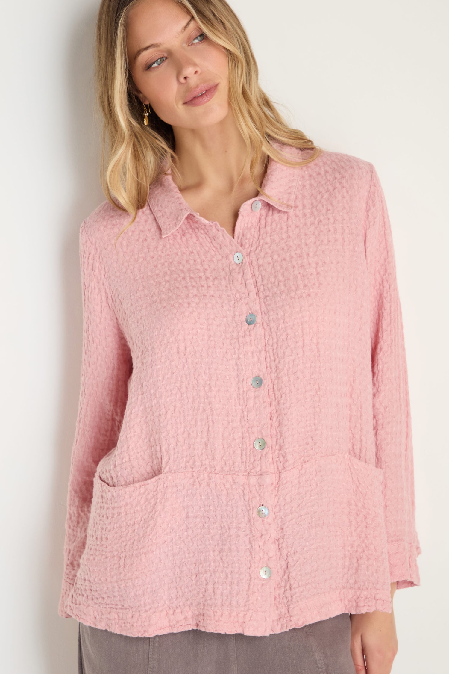 A woman stands against a plain light background wearing the Waffle Linen Pocket Shirt in textured light pink, featuring front pockets—perfect for relaxed layering.