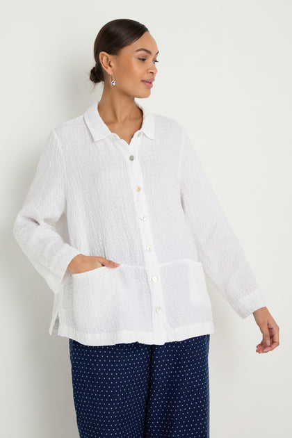 A woman wears the Waffle Linen Pocket Shirt in white with a boxy silhouette and long sleeves, paired with navy blue polka dot pants, standing against a plain light background.