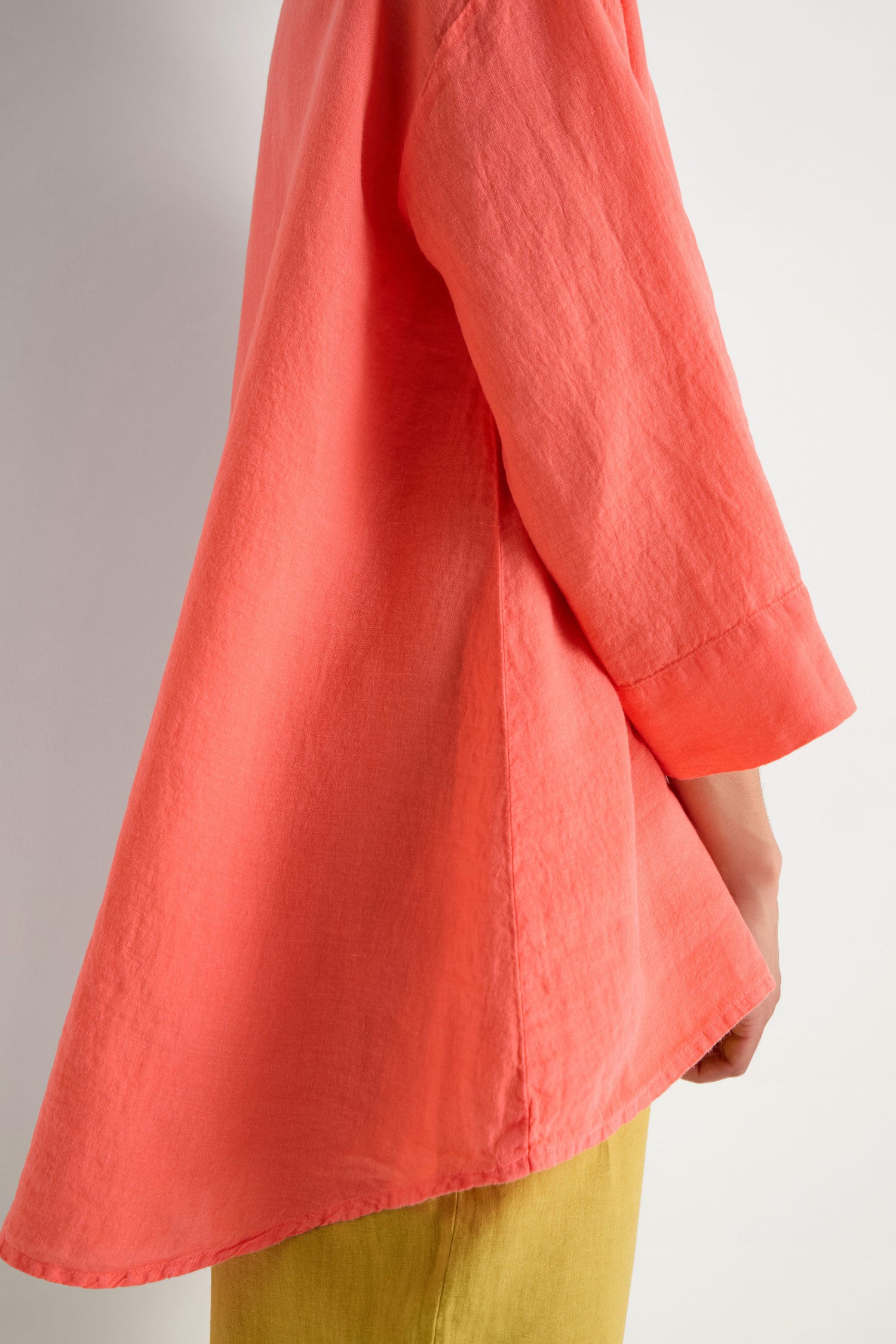 A person wearing the Organza Linen Flared Shirt in loose coral organza linen with long sleeves and yellow pants, shown from shoulder to thigh against a plain background.