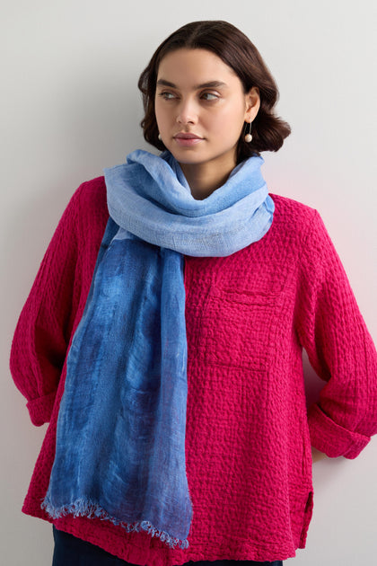 A person wearing a pink textured top and the Sky Linen Mix Scarf, which is sky blue and made of cotton and linen, stands against a light background looking to the side.