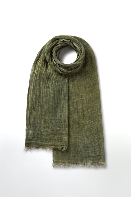 The Woven Linen Scarf, made from 100% linen with a raw-edge finish, is displayed textured and green on a white background, folded at the top.