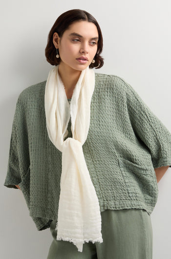 A person with short hair wears a textured green outfit and a Woven Linen Scarf with raw-edge finish, standing against a light gray background.