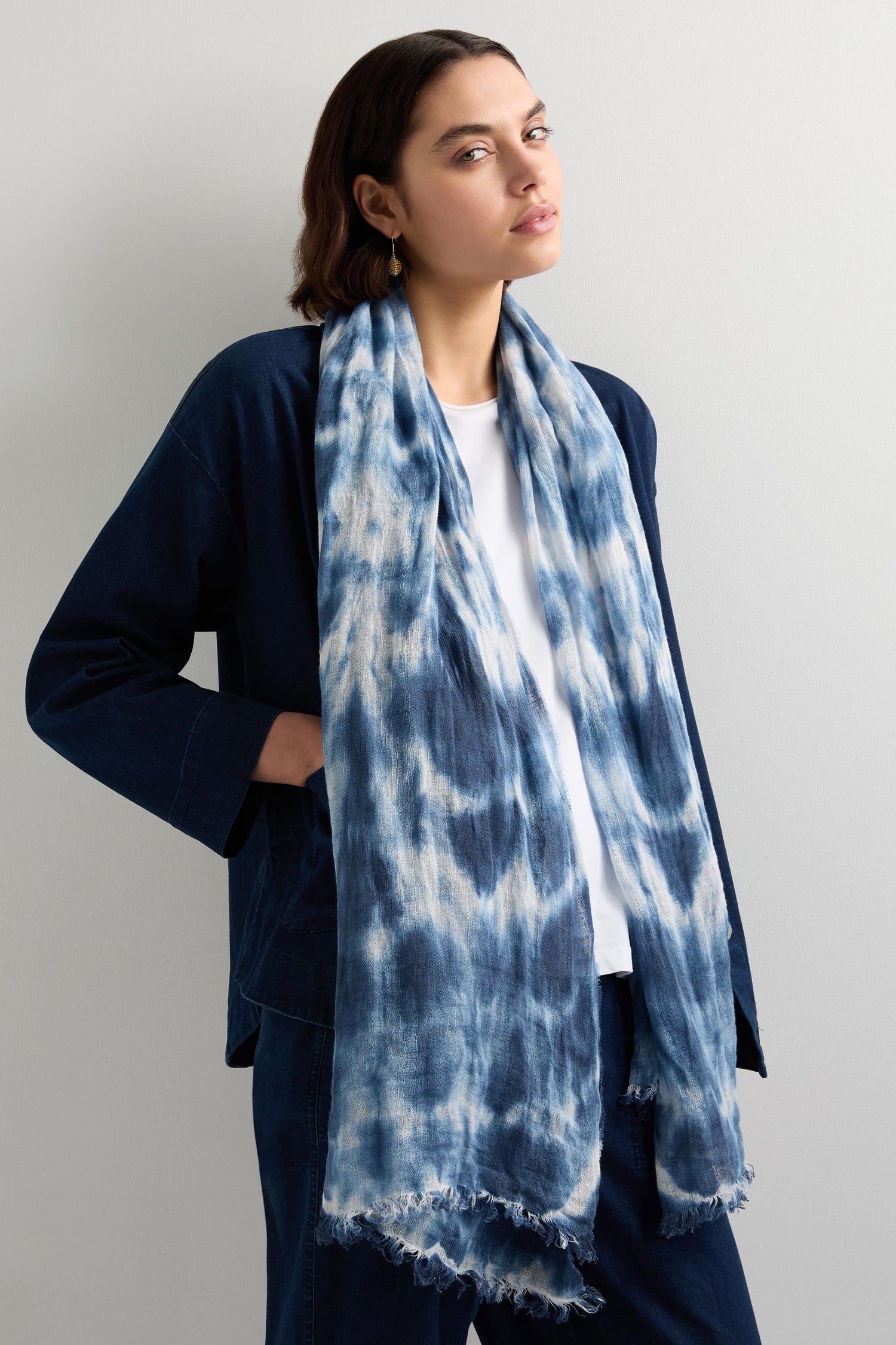 A person is wearing a Tie Dye Linen Scarf in indigo blue with a dark jacket and pants, set against a neutral background.