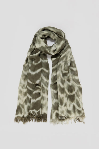 The Sparkle Tie Dye Linen Mix Scarf, in a khaki green and cream pattern, is neatly folded on a plain gray background, highlighting its elegant linen and cotton blend.