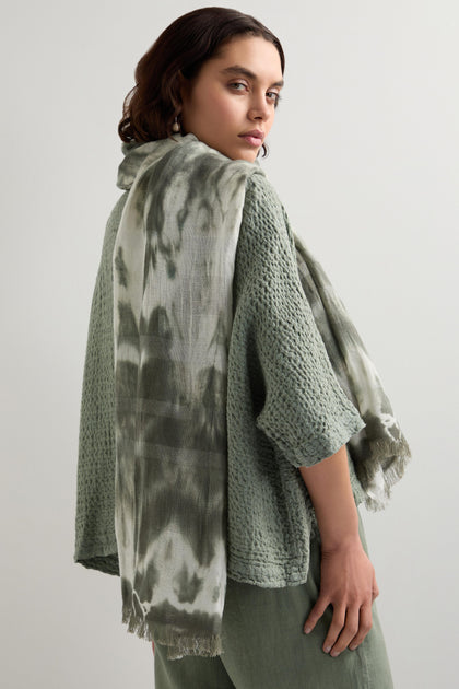 A woman in a textured green linen and cotton outfit drapes a Sparkle Tie Dye Linen Mix Scarf over her shoulder, standing against a neutral background.