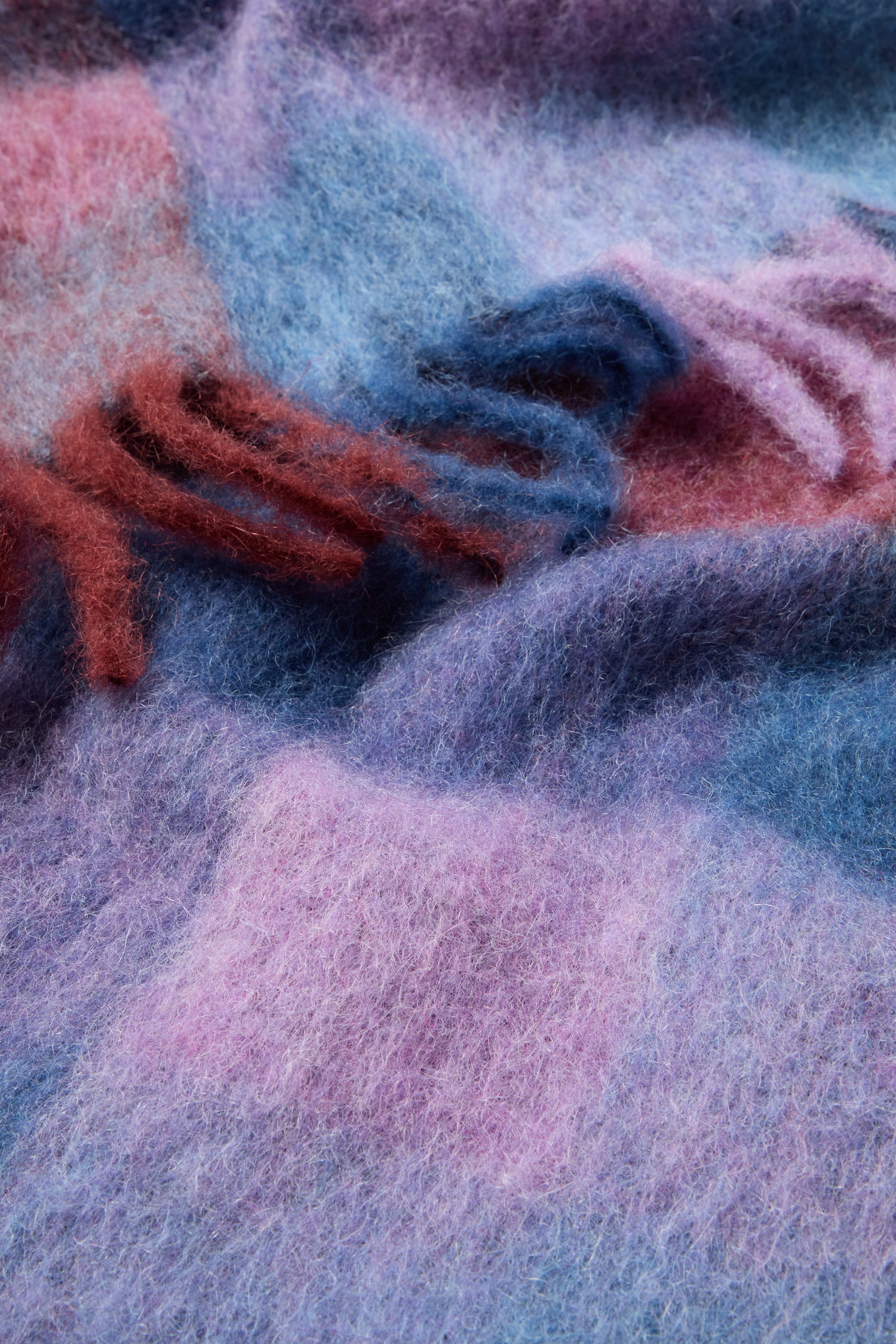 Close-up of a multicolored, fuzzy fabric featuring shades of blue, purple, and pink that evoke the soft and woolly textures of a luxurious mohair wool blend as seen in the Check Tassel Scarf.