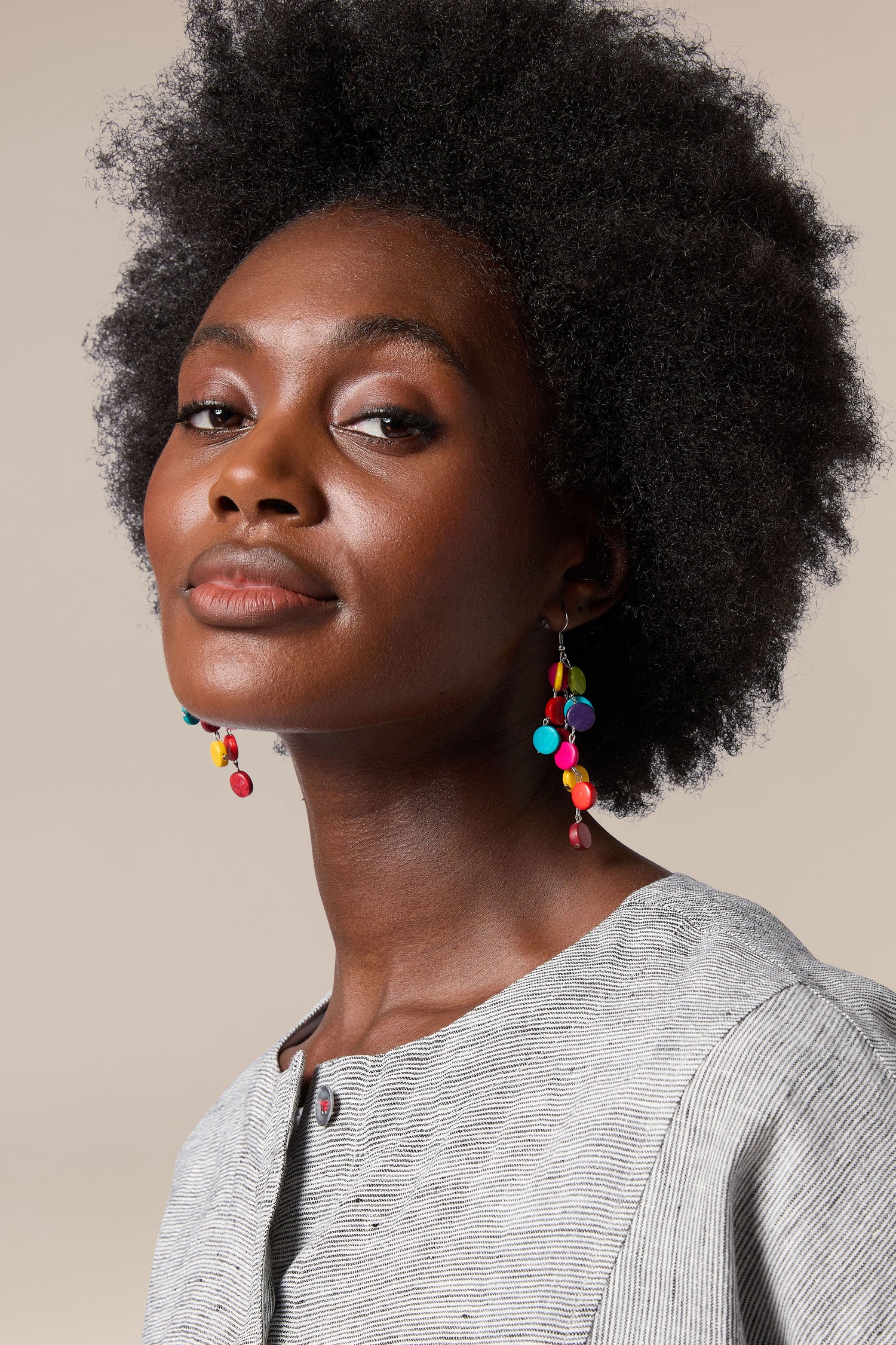 A black woman with afro hair wearing handcrafted, colorful Cascade Earrings made by local artisans.