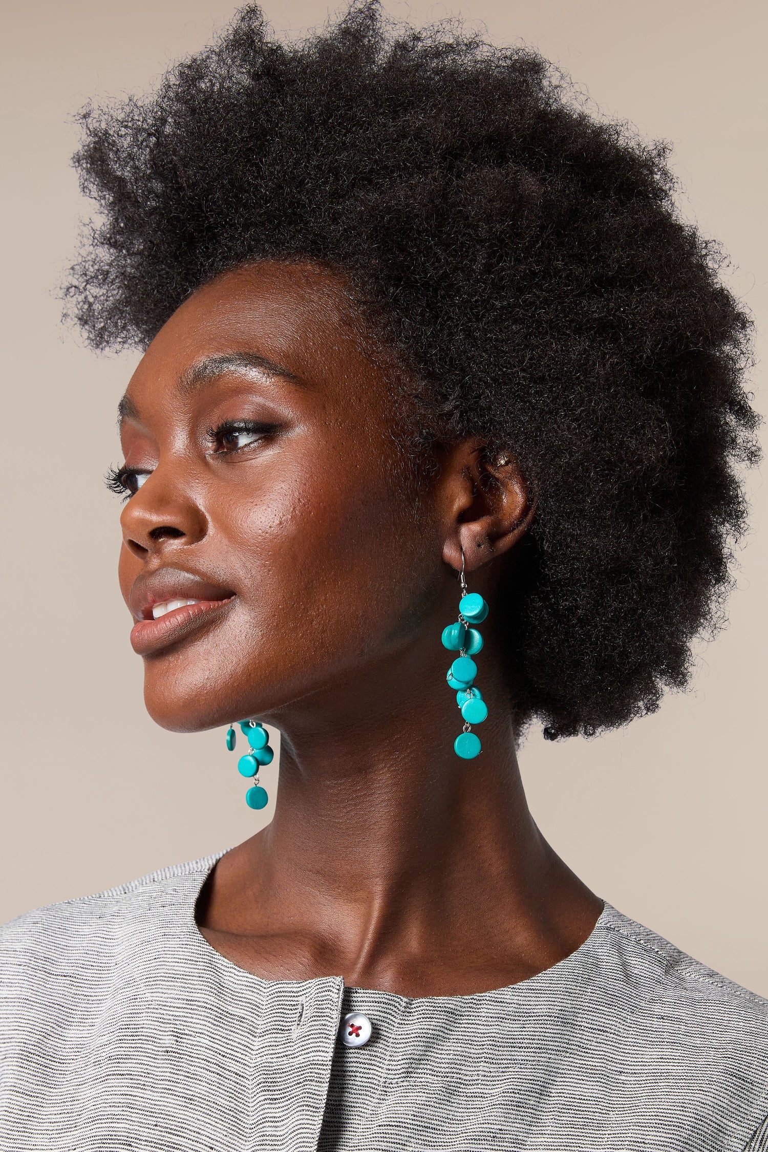 A black woman with afro hair wearing colourful, handcrafted Cascade Earrings made by local artisans.