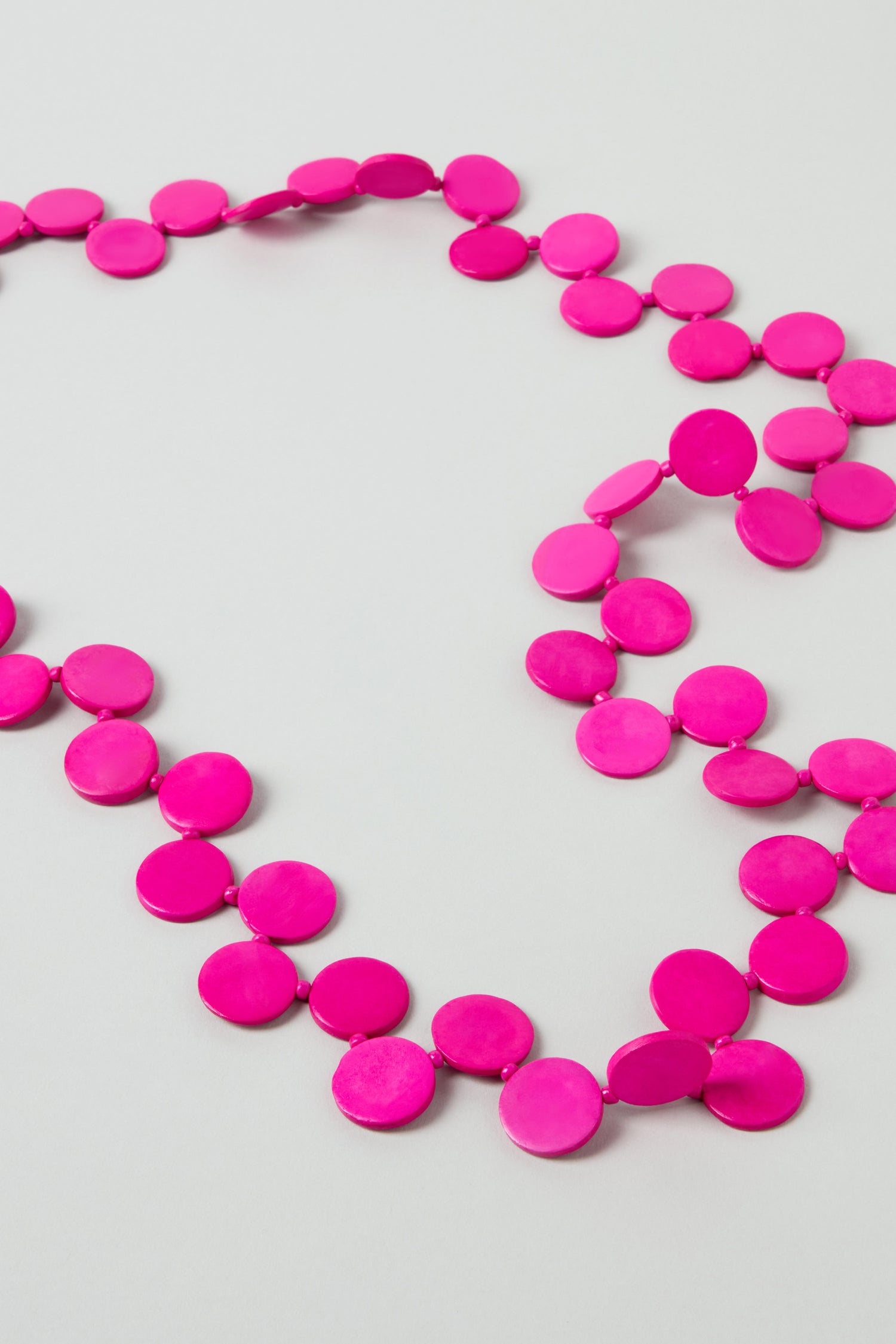 The Long Strand Coco Disc Necklace features handcrafted bright pink flat circular beads, beautifully arranged on a light surface.