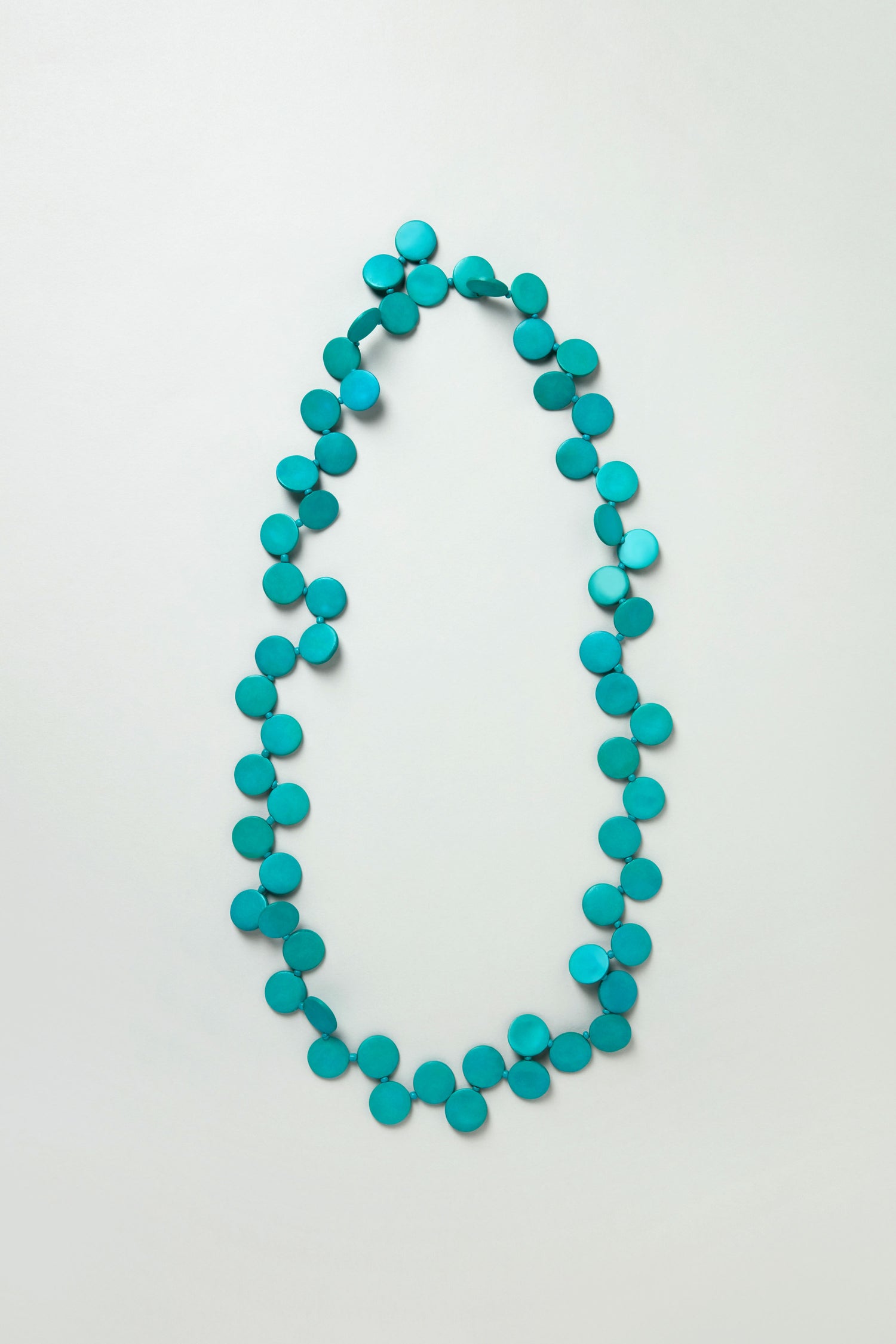 The Long Strand Coco Disc Necklace features handcrafted, flat round beads arranged in a single strand and displayed in an oval shape on a light background.