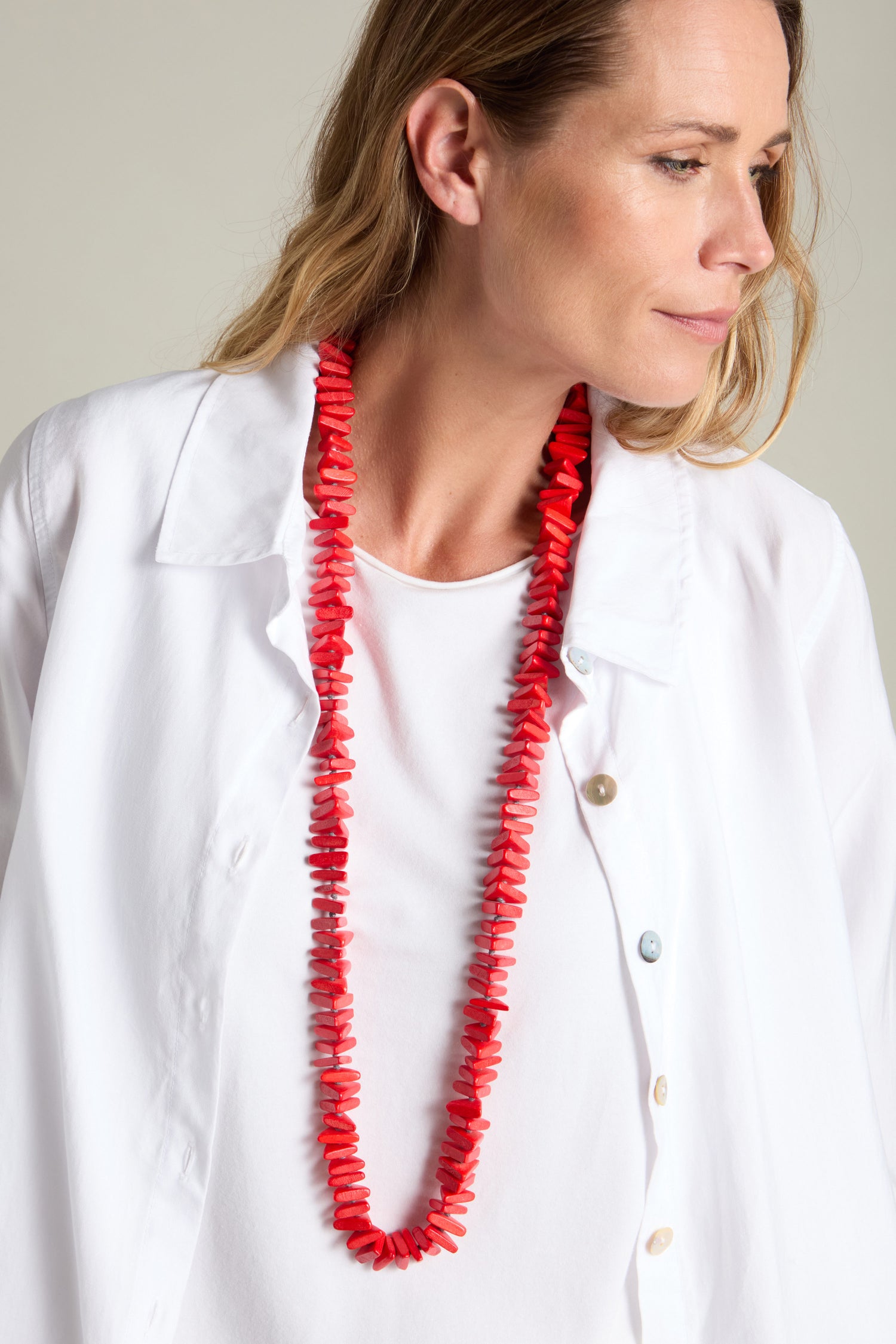 Person wearing a white shirt and the Mini Triangles Wooden Necklace, a long red beaded accessory featuring delicate mini triangles, looking to the right.