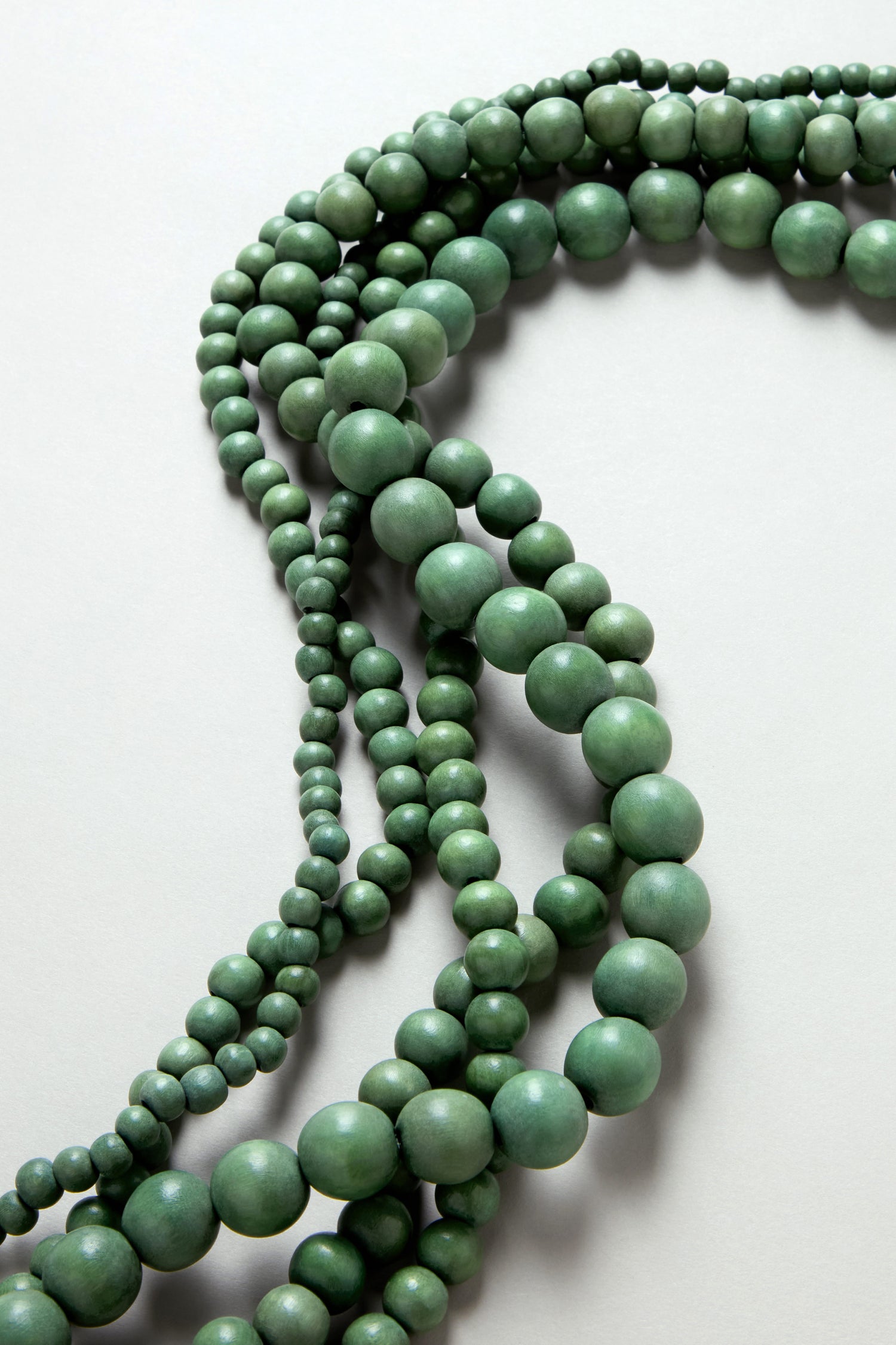 The Statement Bead Necklace features multiple strands of round green beads in varying sizes, displayed on a light gray surface to highlight their natural elegance.