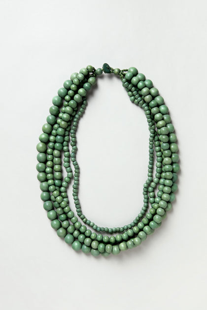 The Statement Bead Necklace features round green sustainable wood beads in assorted sizes, displayed flat on a plain white background.