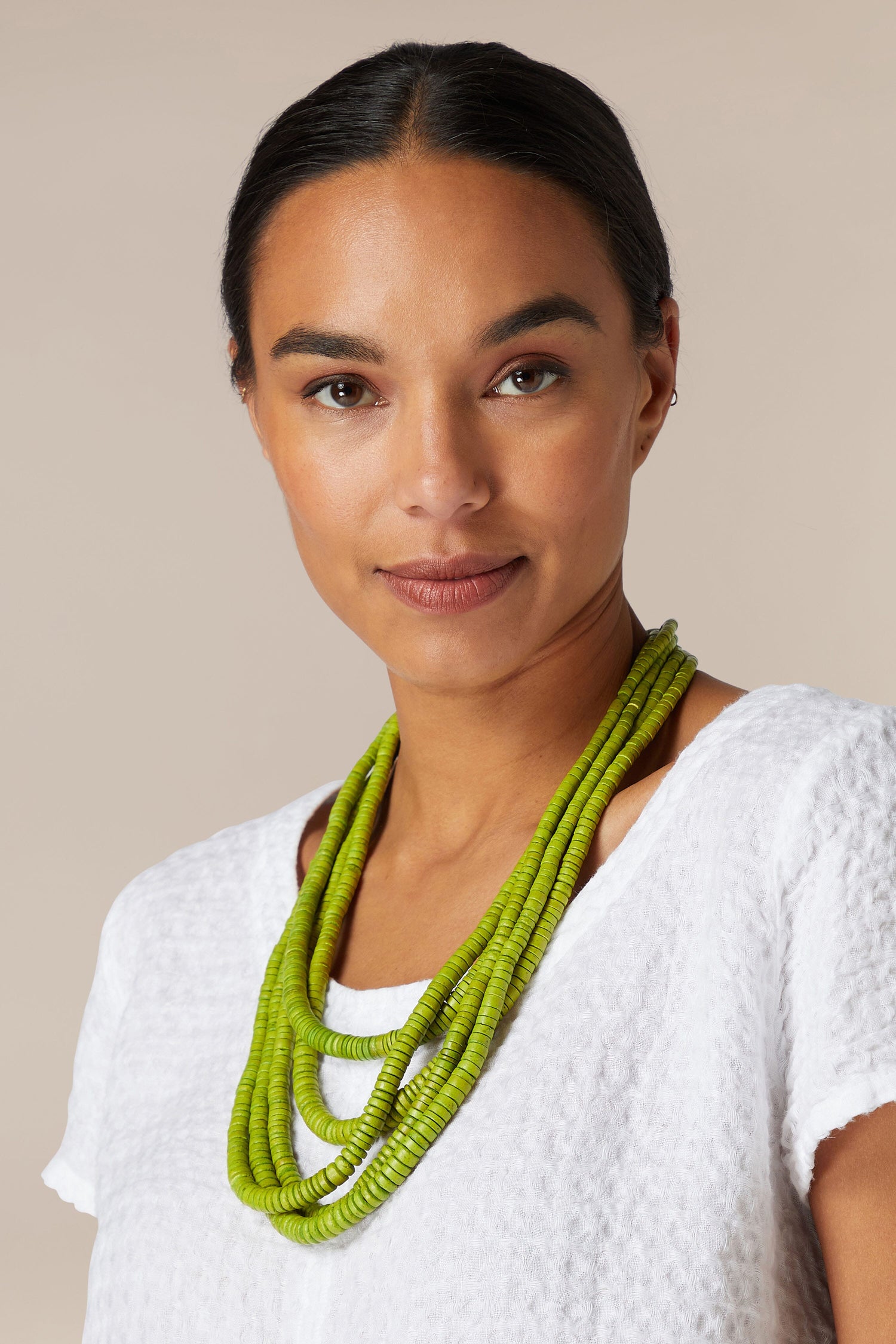 A woman wearing a green Coconut Shell Disc Necklace made of coconut shell beads.