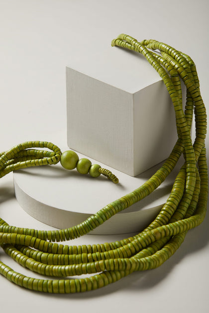 A Coconut Shell Disc Necklace with green coconut shell beads on top of a white surface.