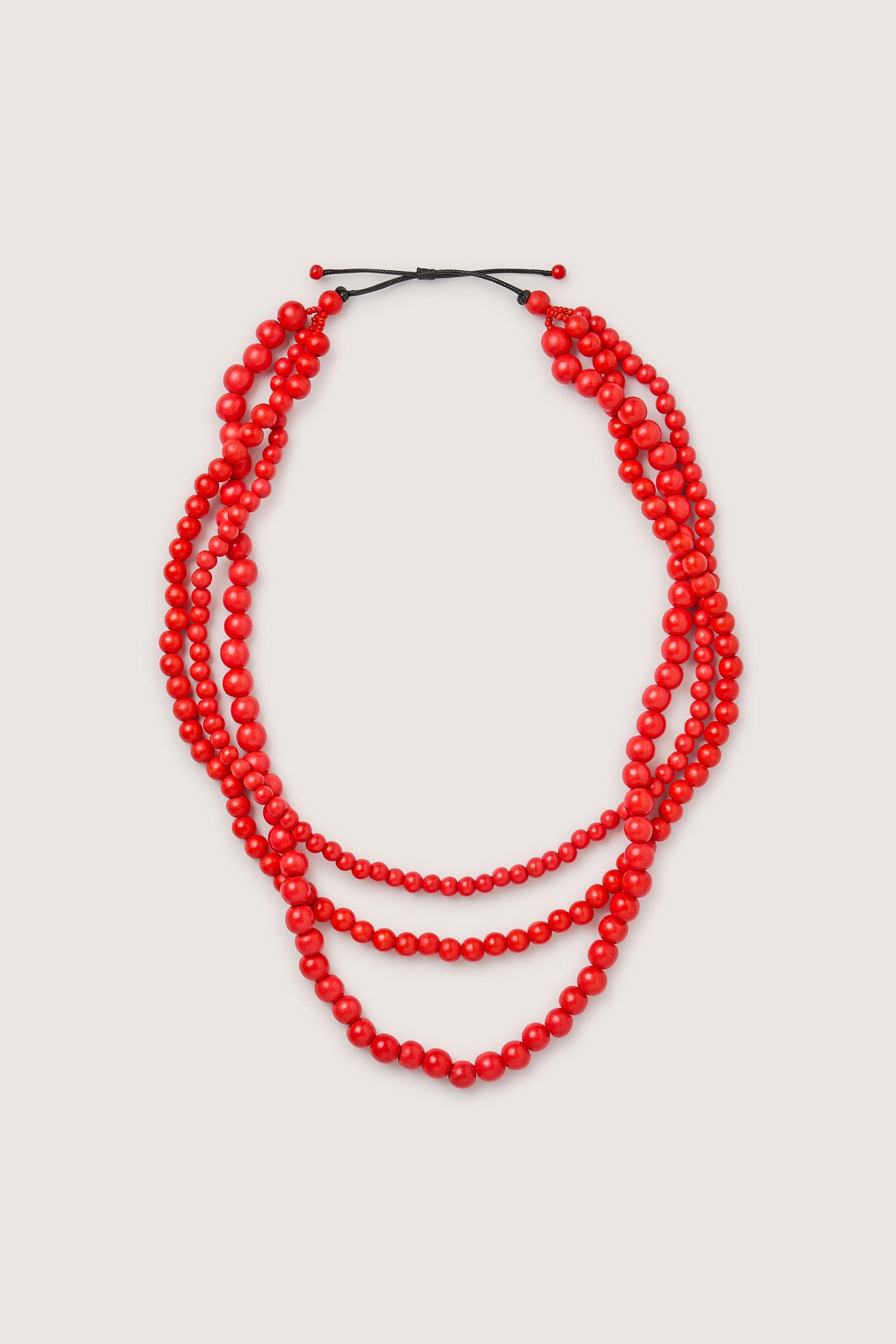 The Wooden Cascade Spheres Necklace, inspired by the Philippines, is a handmade piece featuring three layers of red beads joined at the back with black adjustable knots.