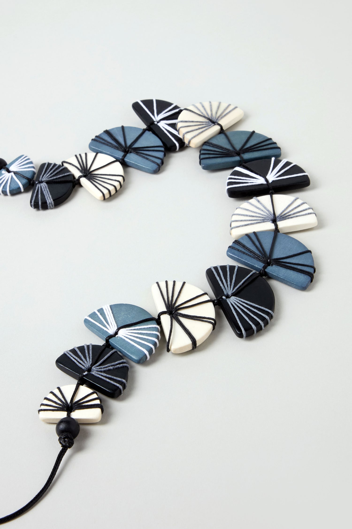 The Fan Necklace features fan-shaped beads in blue, black, and white with linear patterns, made from sustainable Pangantuan wood and strung on a black cord.