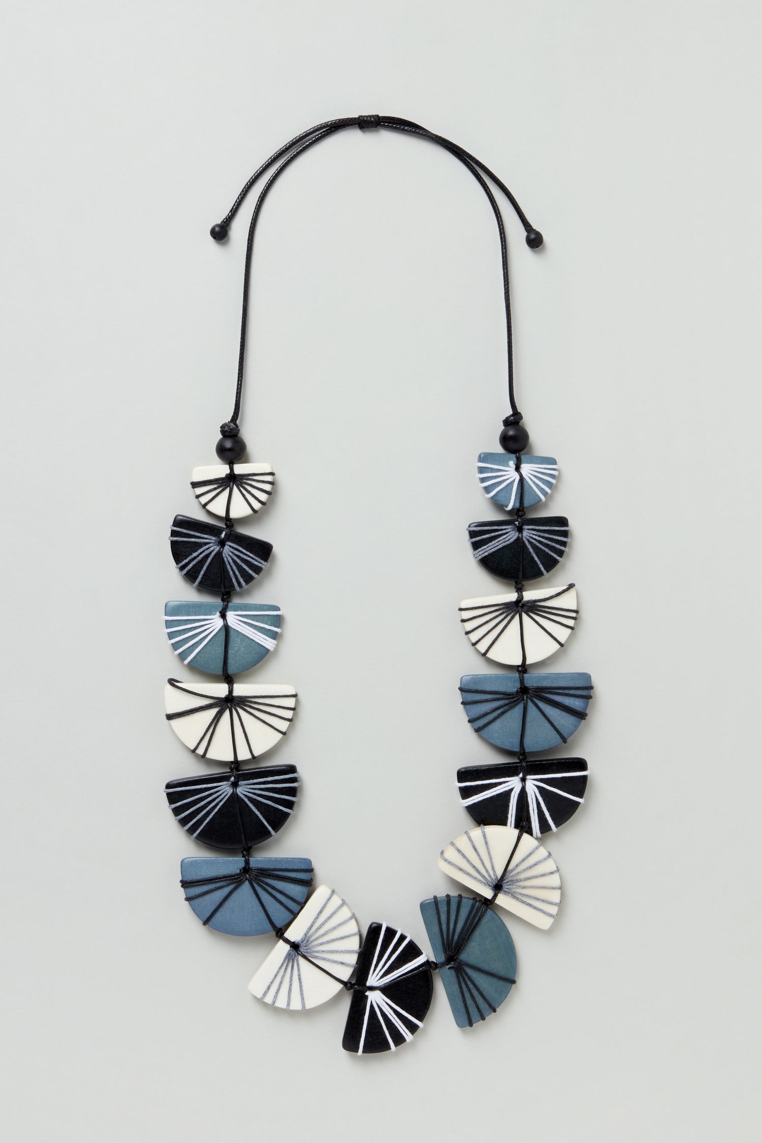 The Fan Necklace (LFHC0324), a blue, black, and white geometric beaded necklace with a cord and bead closure, is displayed on a light background with "Coming Soon" repeatedly overlaid on the image.