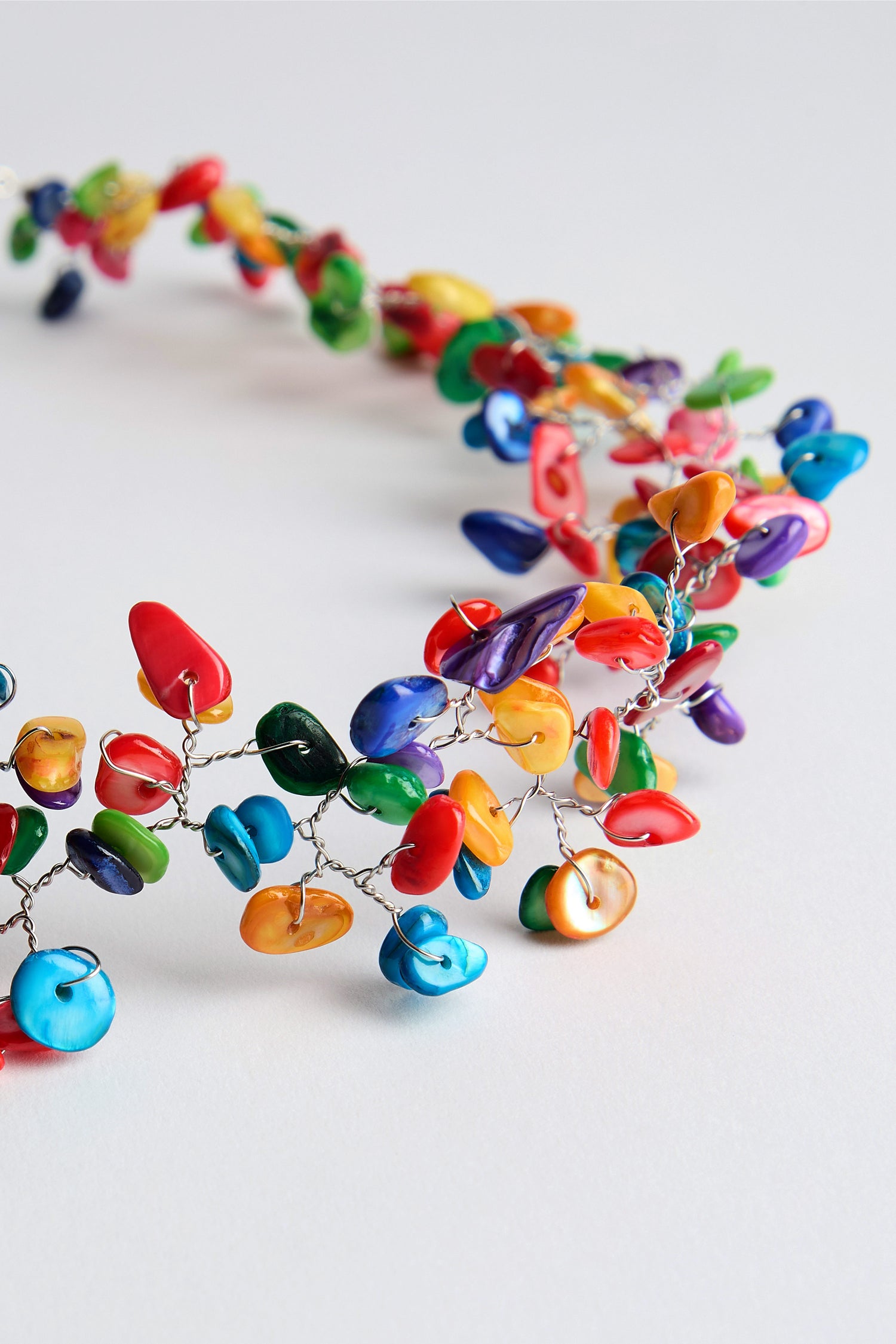 The Rainbow Rivershell Necklace is a striking accessory with handcrafted river shell beads in a scattered design on thin wire, featuring variously shaped, multi-colored stones that add vibrant colors to enhance any outfit.