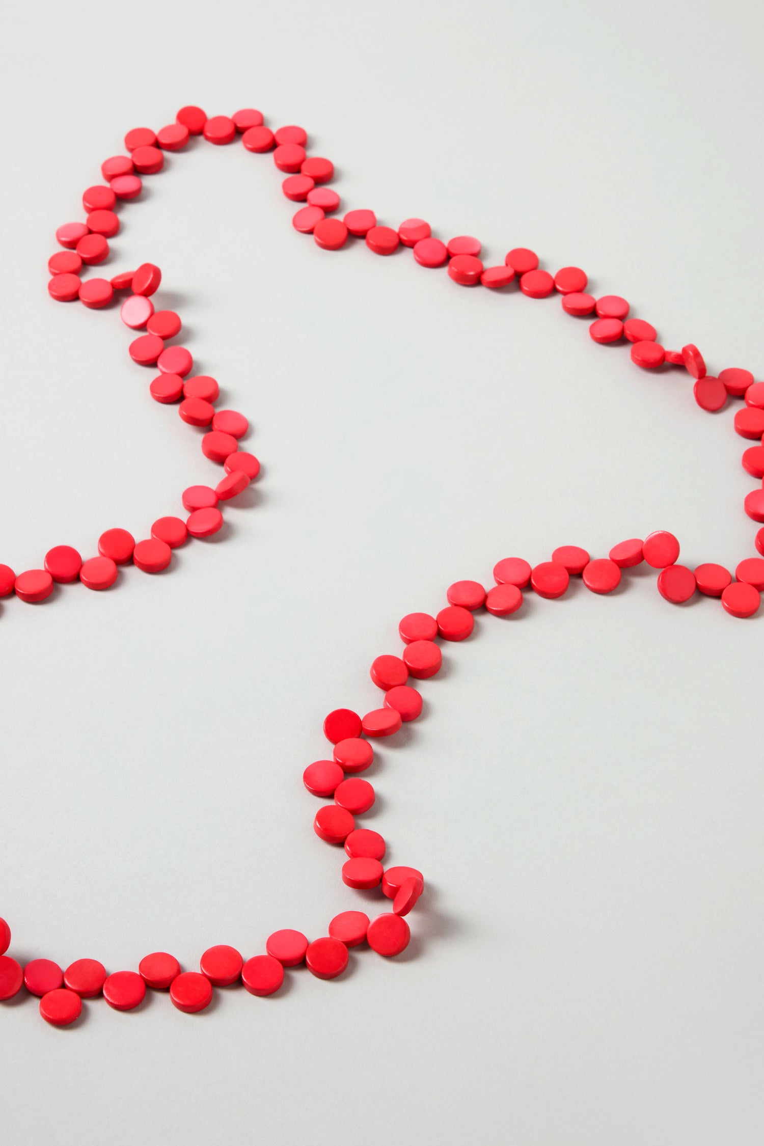The Single Strand Coco Necklace, a long handcrafted piece, is arranged in loose wavy loops on a flat, light-colored surface.