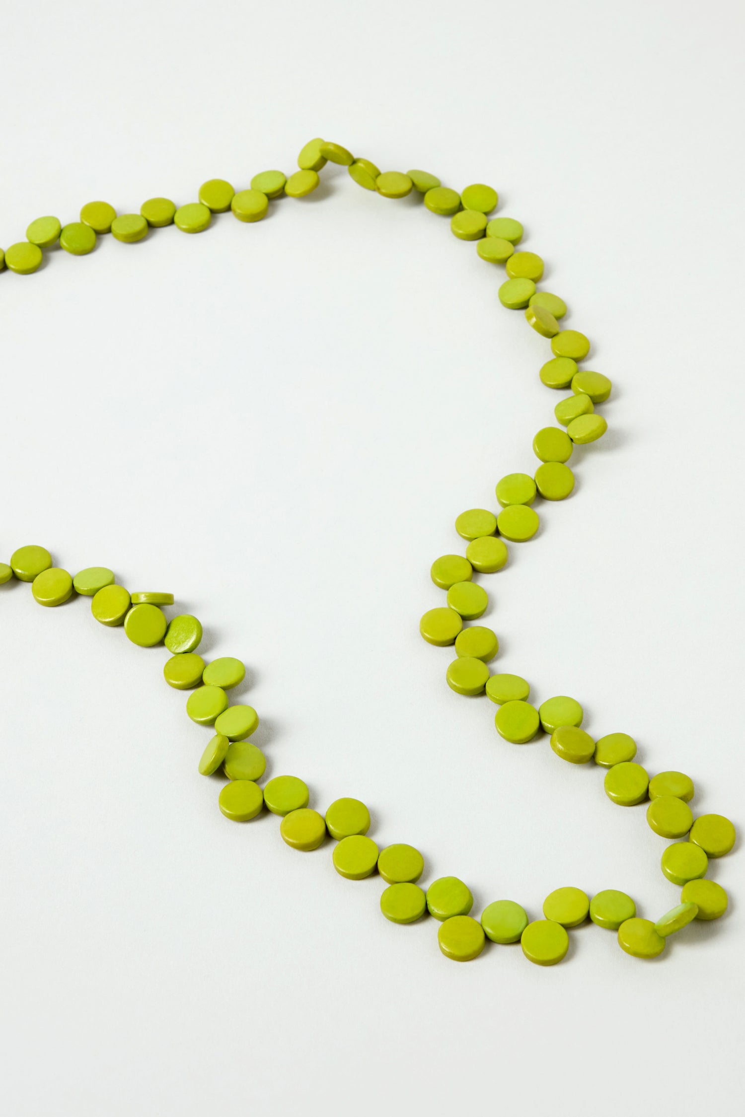 The Single Strand Coco Necklace features small, round, flat green beads and is displayed on a white surface—a beautiful, handcrafted, and lightweight accessory to suit any style.