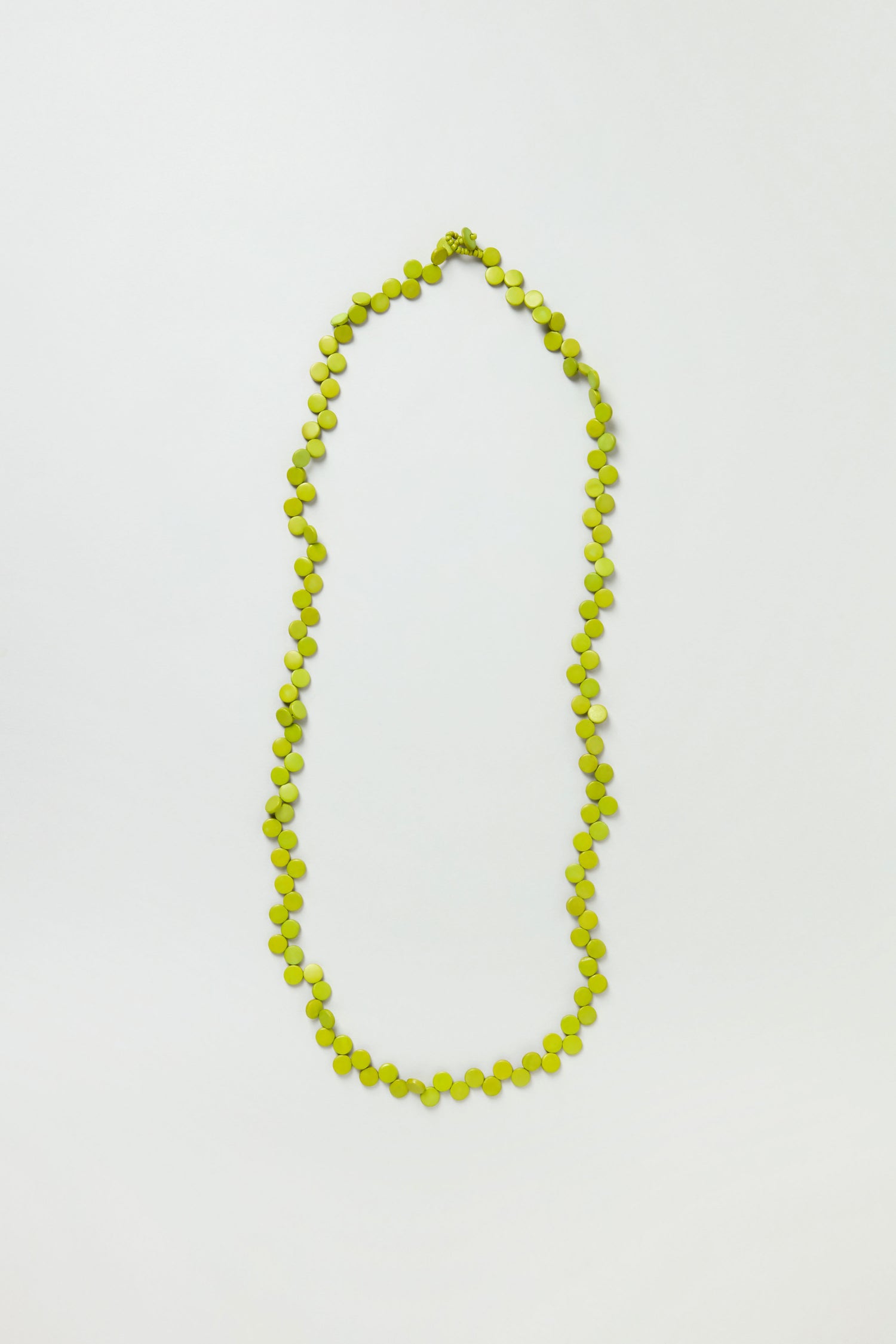 The Single Strand Coco Necklace is a handcrafted piece featuring small, round, green beads in a lightweight design, elegantly displayed on a plain white background.