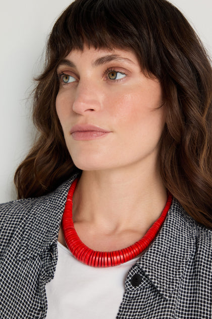 A woman with wavy brown hair wears a black and white checkered shirt, a white top, and the Graduated Coco Disc Necklace handcrafted in the Philippines, looking slightly to the side.