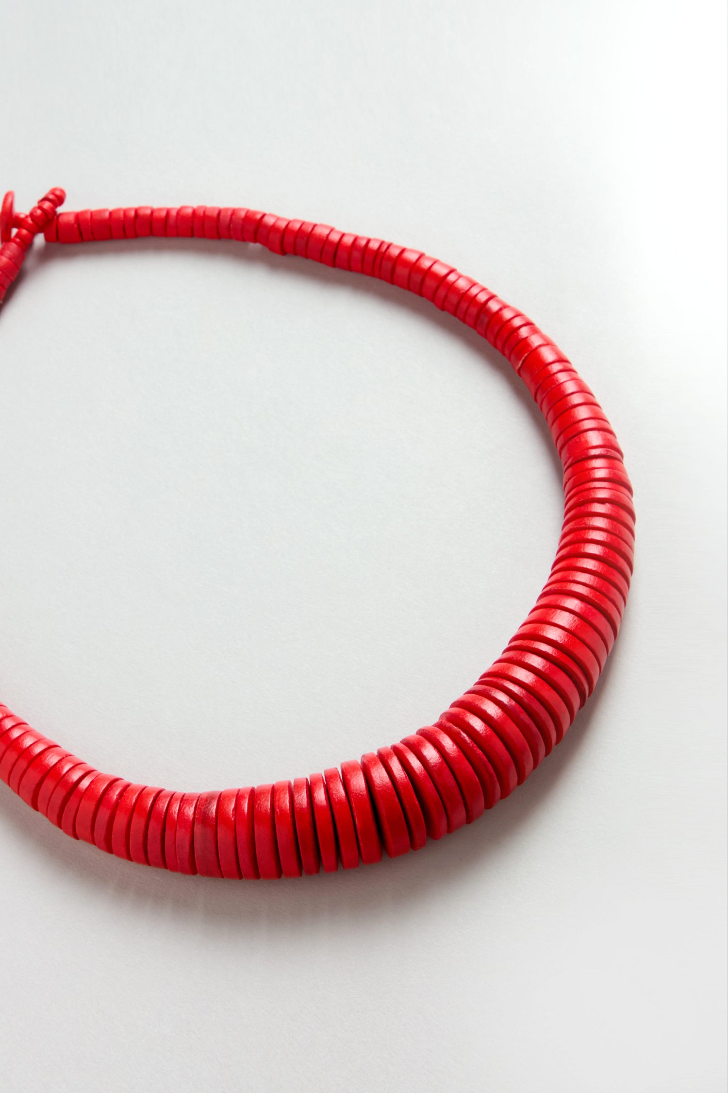 The Graduated Coco Disc Necklace is handcrafted in the Philippines with flat, round red beads strung closely together, forming a thick, circular shape.