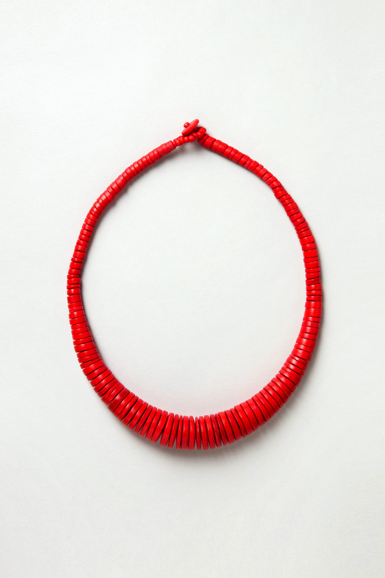 The Graduated Coco Disc Necklace is handcrafted in the Philippines, featuring uniformly shaped flat red beads strung in a single loop, and is showcased against a plain light background.
