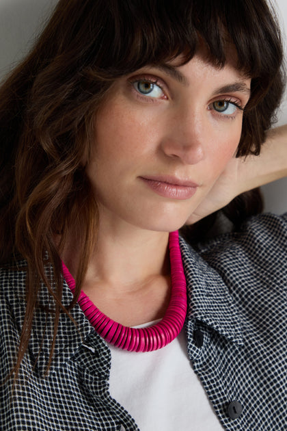 A woman with wavy brown hair wears a black-and-white checkered shirt, a white top, and a Graduated Coco Disc Necklace handcrafted and ethically sourced from the Philippines as she looks at the camera.