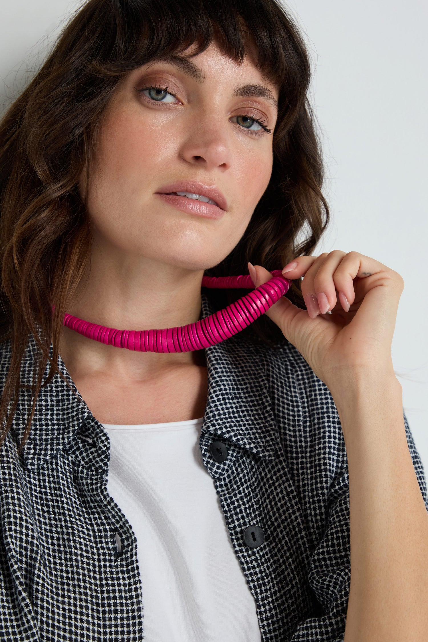 Woman with wavy brown hair wearing a black and white checkered shirt, white top, and the Graduated Coco Disc Necklace—handcrafted in the Philippines—holding the necklace near her neck.