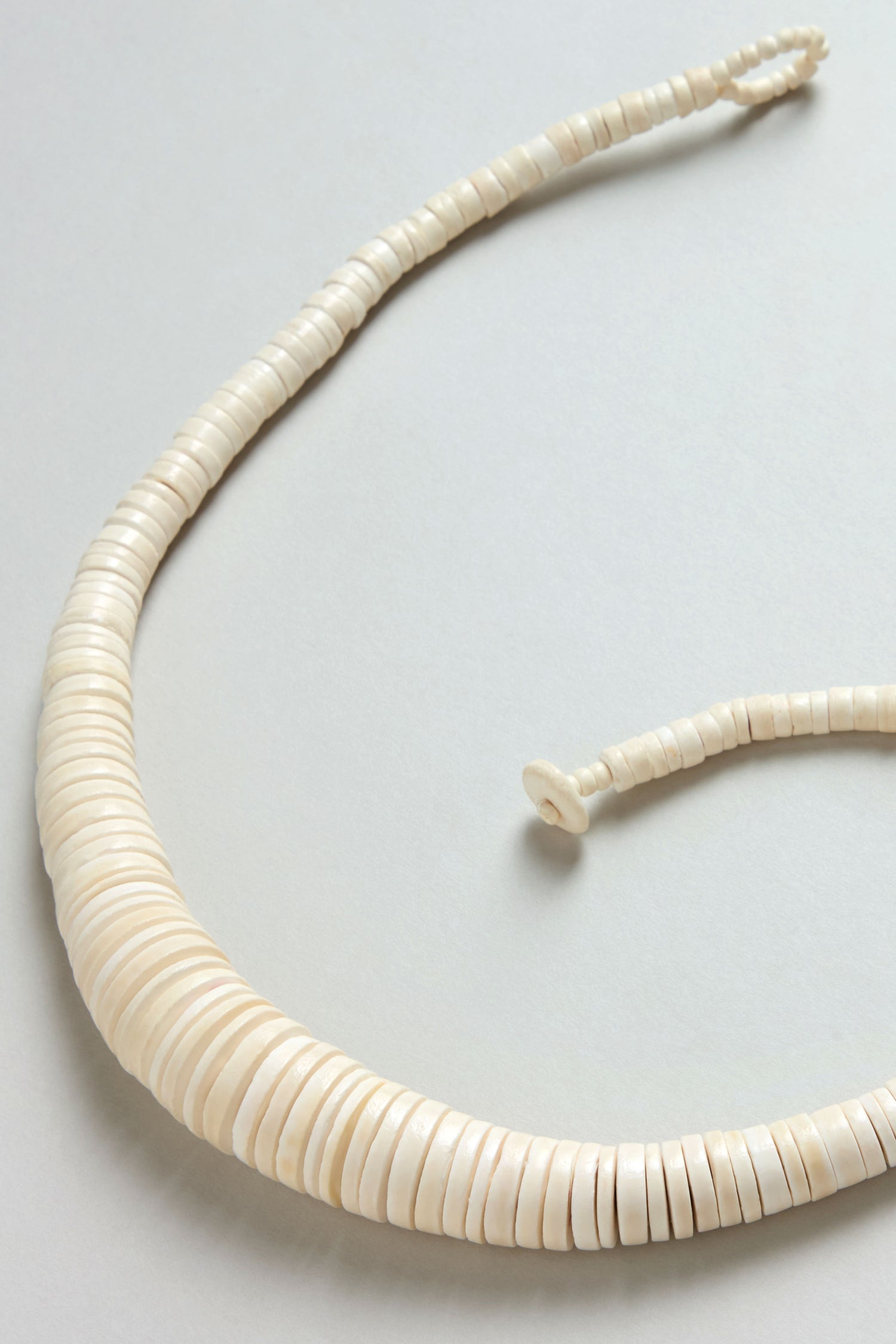 A close-up of the Graduated Coco Disc Necklace, handcrafted in the Philippines from ethically sourced flat white shell beads, beautifully arranged in a single strand against a light background.