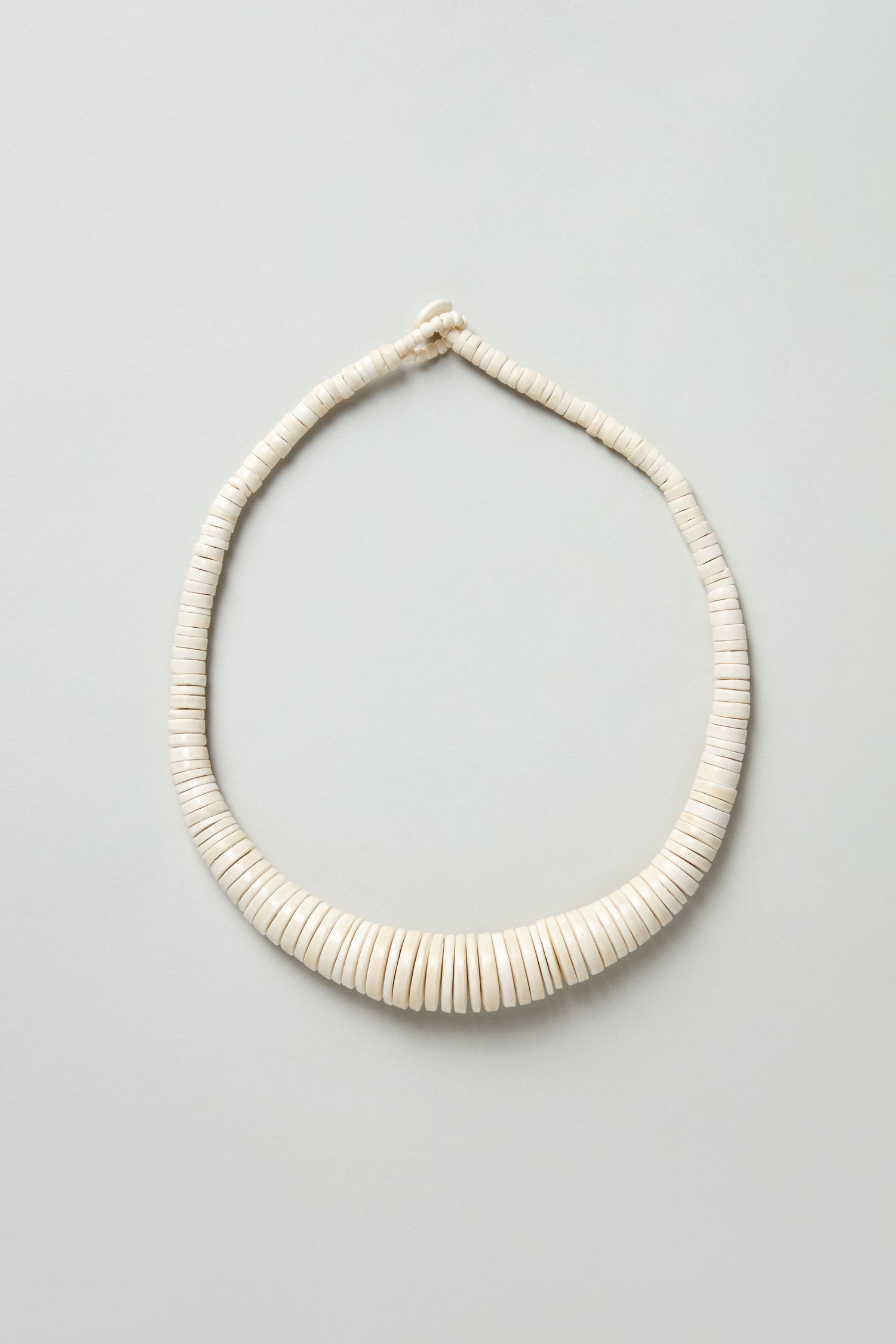The Graduated Coco Disc Necklace, handcrafted in the Philippines with evenly spaced, round white beads, is laid flat on a light background. Ethically sourced beads make it a beautiful and responsible accessory.