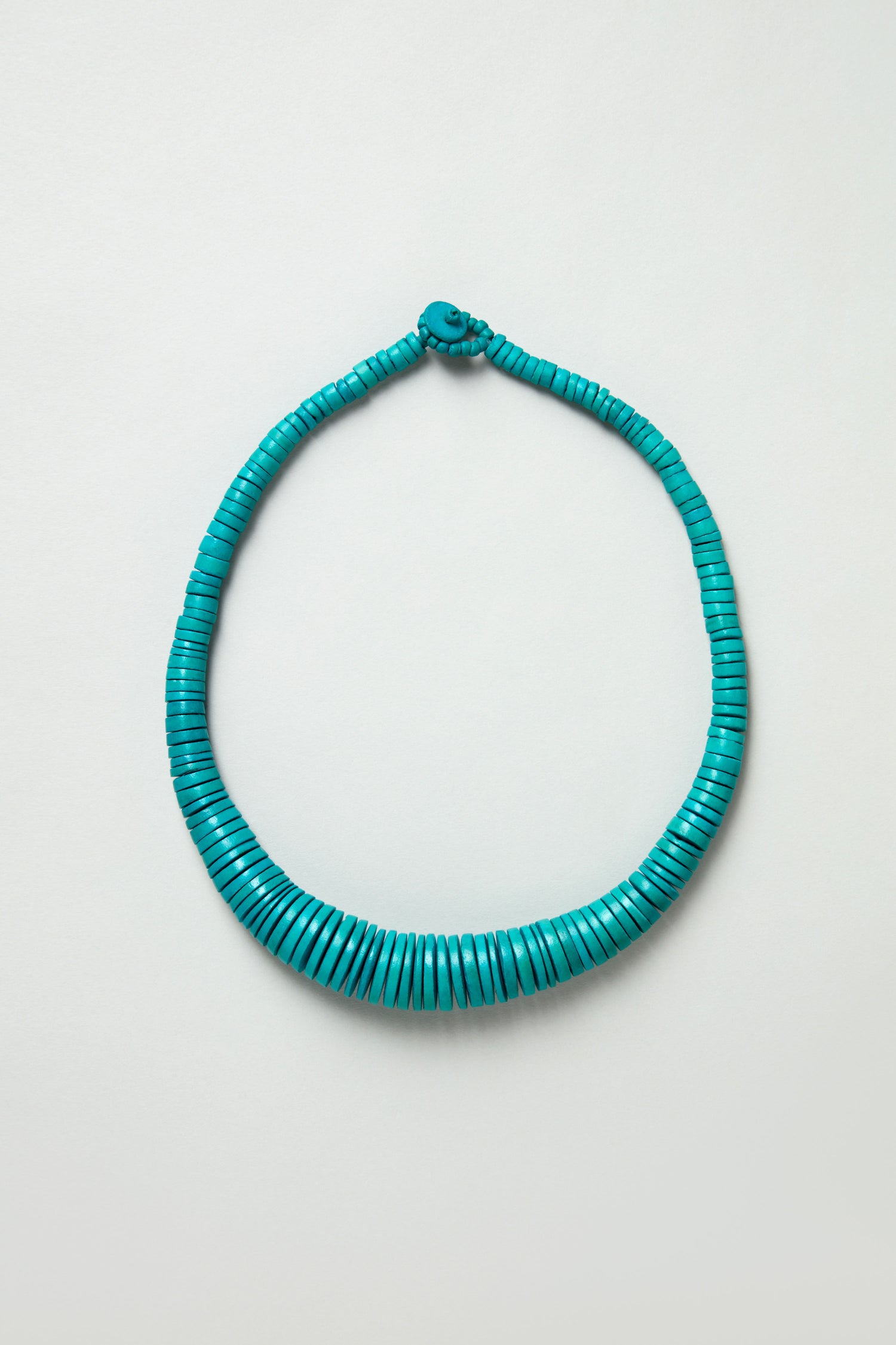 The Graduated Coco Disc Necklace is handcrafted in the Philippines with turquoise, flat beads arranged in a circular pattern on a light background.
