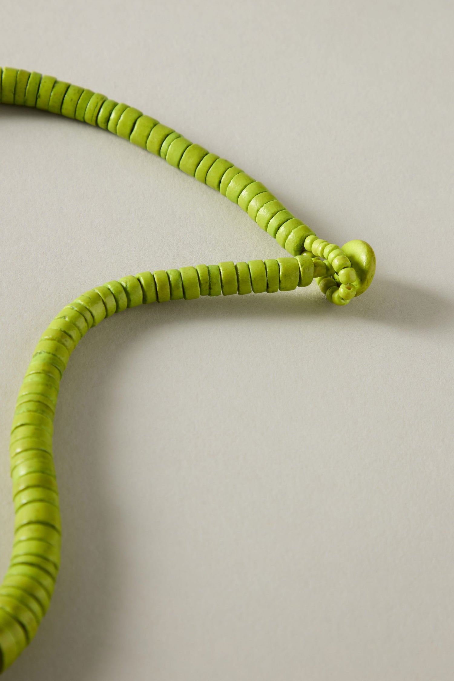 A close-up of the Graduated Coco Disc Necklace showcases its green bead design with small discs, expertly crafted in the Philippines and partially knotted on a light gray background.