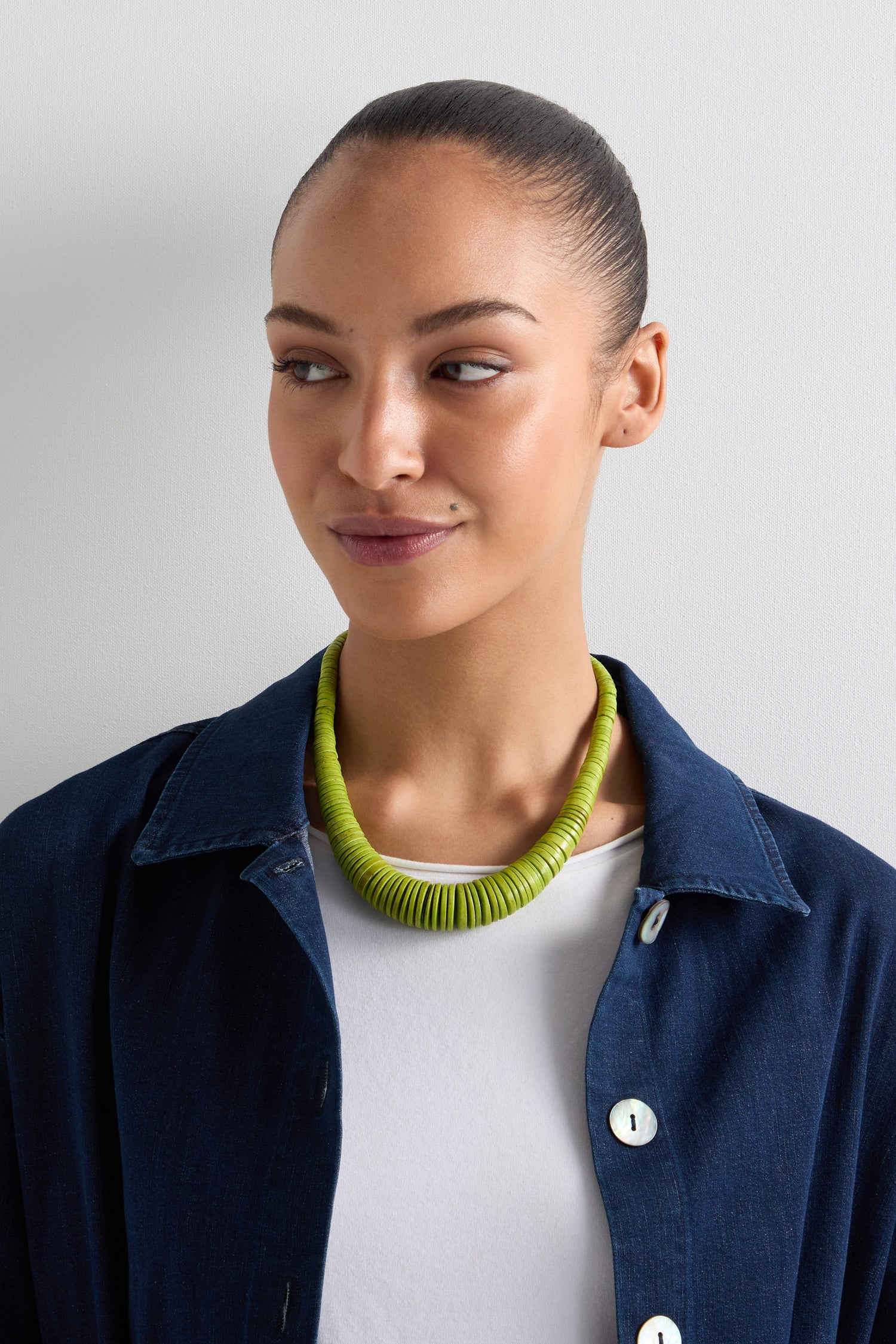 A person in a dark blue jacket and white top wears the Graduated Coco Disc Necklace, ethically made, showcasing Philippines craftsmanship, against a plain light background.