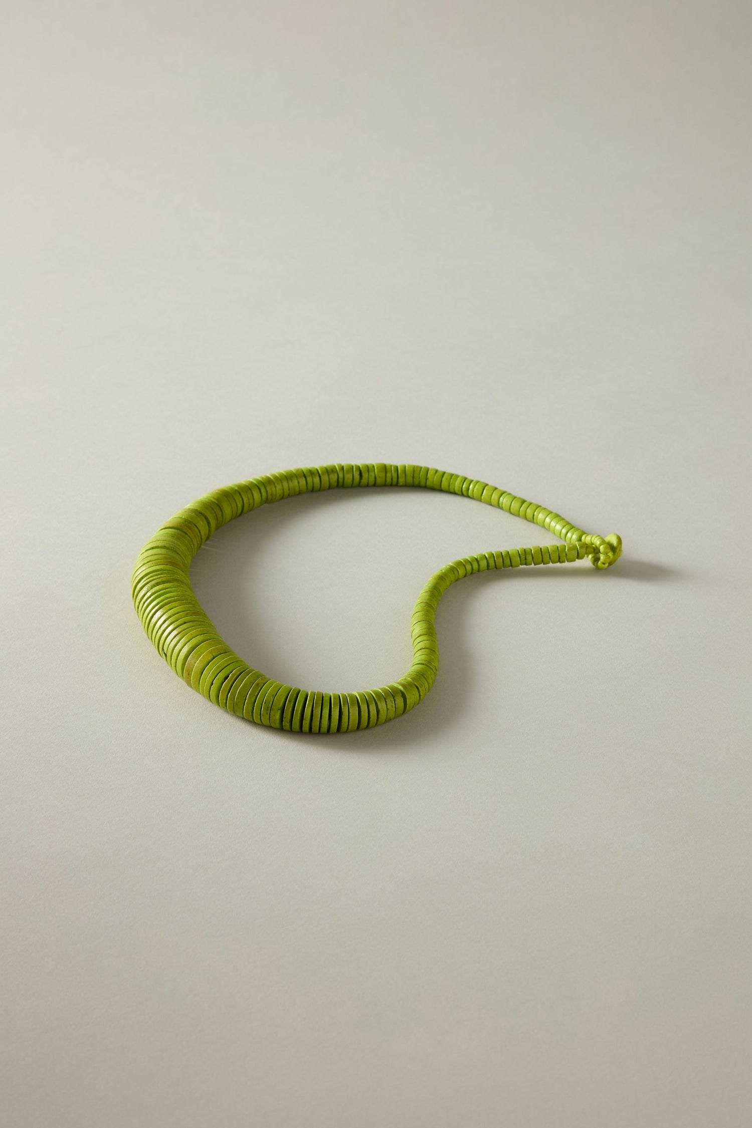 A coiled green phone cord, reminiscent of the Graduated Coco Disc Necklace's bead design inspired by Philippine craftsmanship, is arranged in an irregular loop on a plain light gray surface.