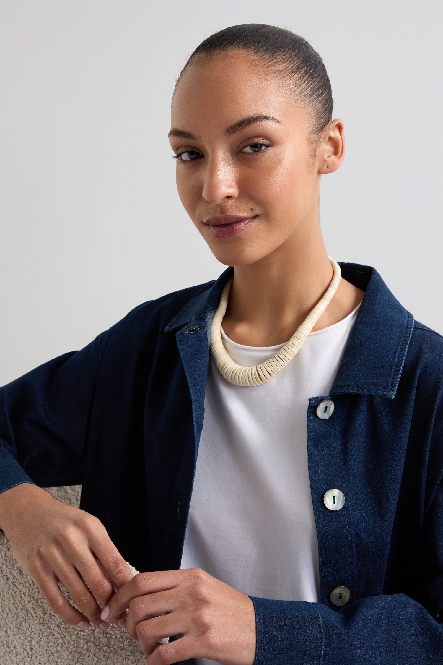 A person wearing a navy button-up shirt, a white t-shirt, and the Graduated Coco Disc Necklace—highlighting Filipino craftsmanship—sits smiling with a hand on a surface.